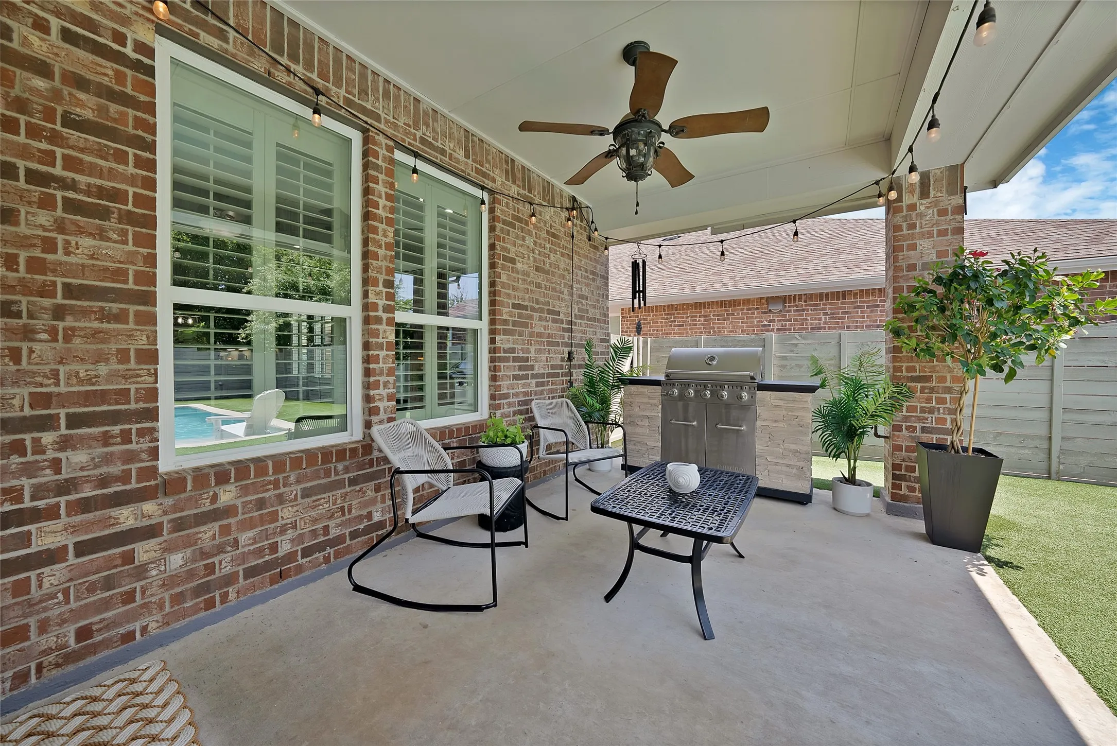 Covered patio featuring a ceiling fan, string lighting, and an outdoor kitchen with a built-in grill