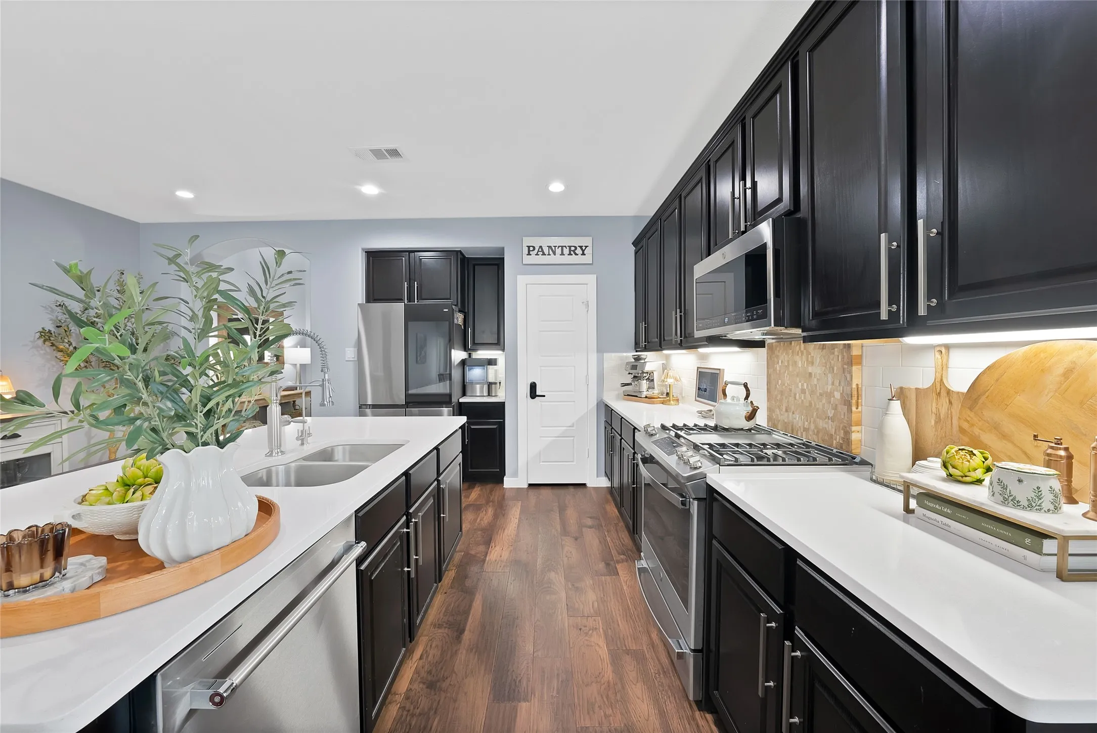 Modern kitchen featuring dark cabinetry with brushed nickel hardware, white countertops, stainless steel appliances, and wood-finish flooring