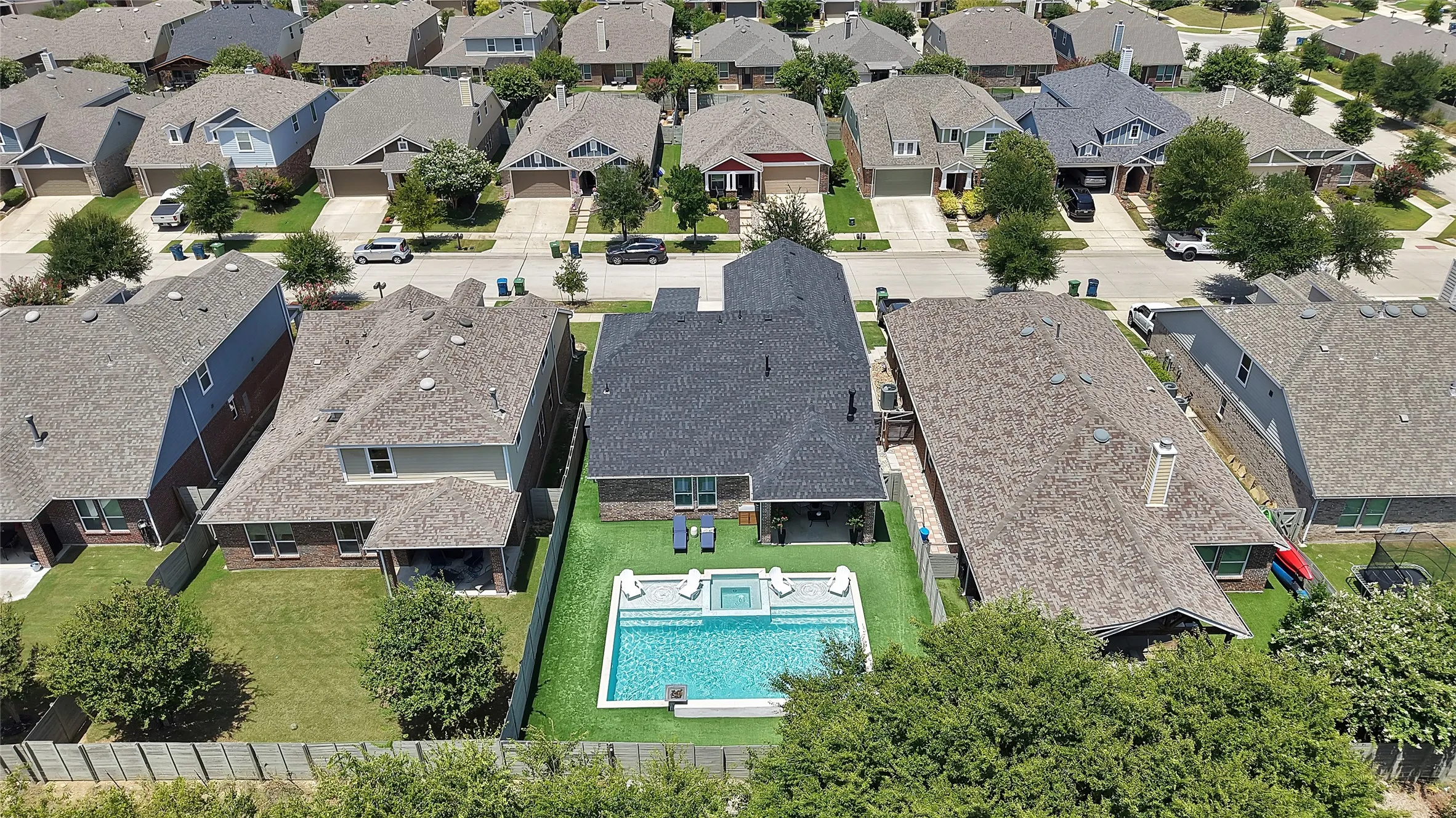 Backyard oasis featuring a rectangular swimming pool with integrated spa, artificial turf surrounding the pool deck, a covered patio, and a privacy fence