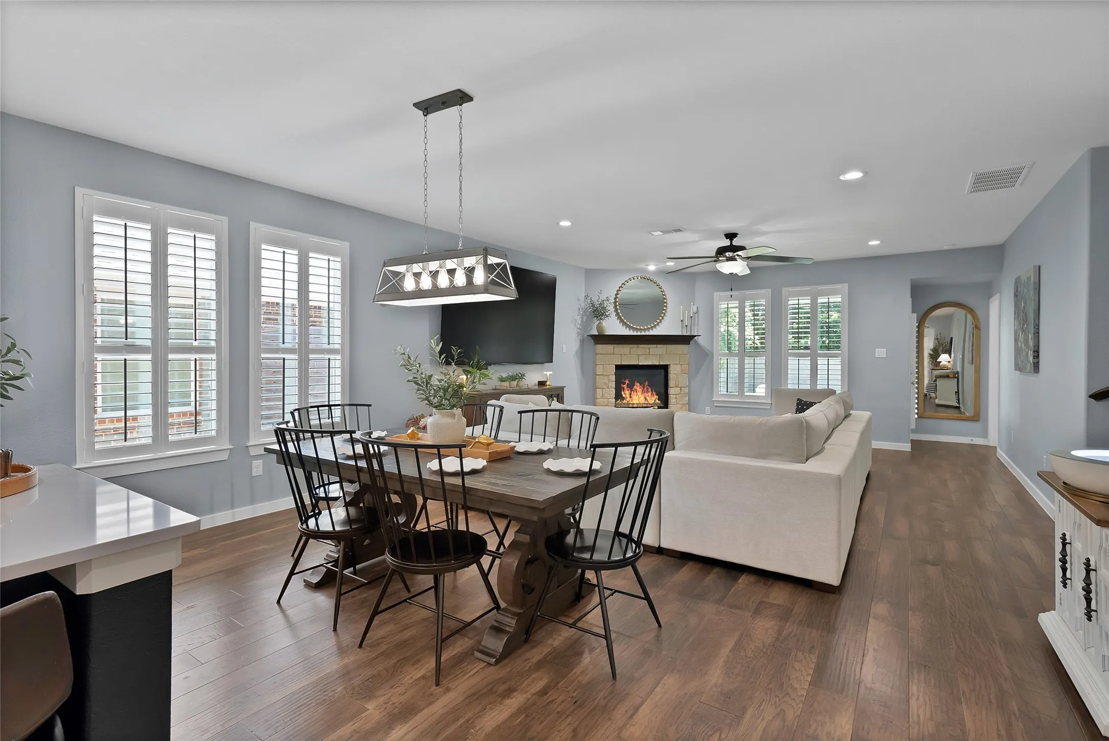 Open-concept living space featuring wood-finish flooring, a stone-faced fireplace with a mantel, and recessed lighting
