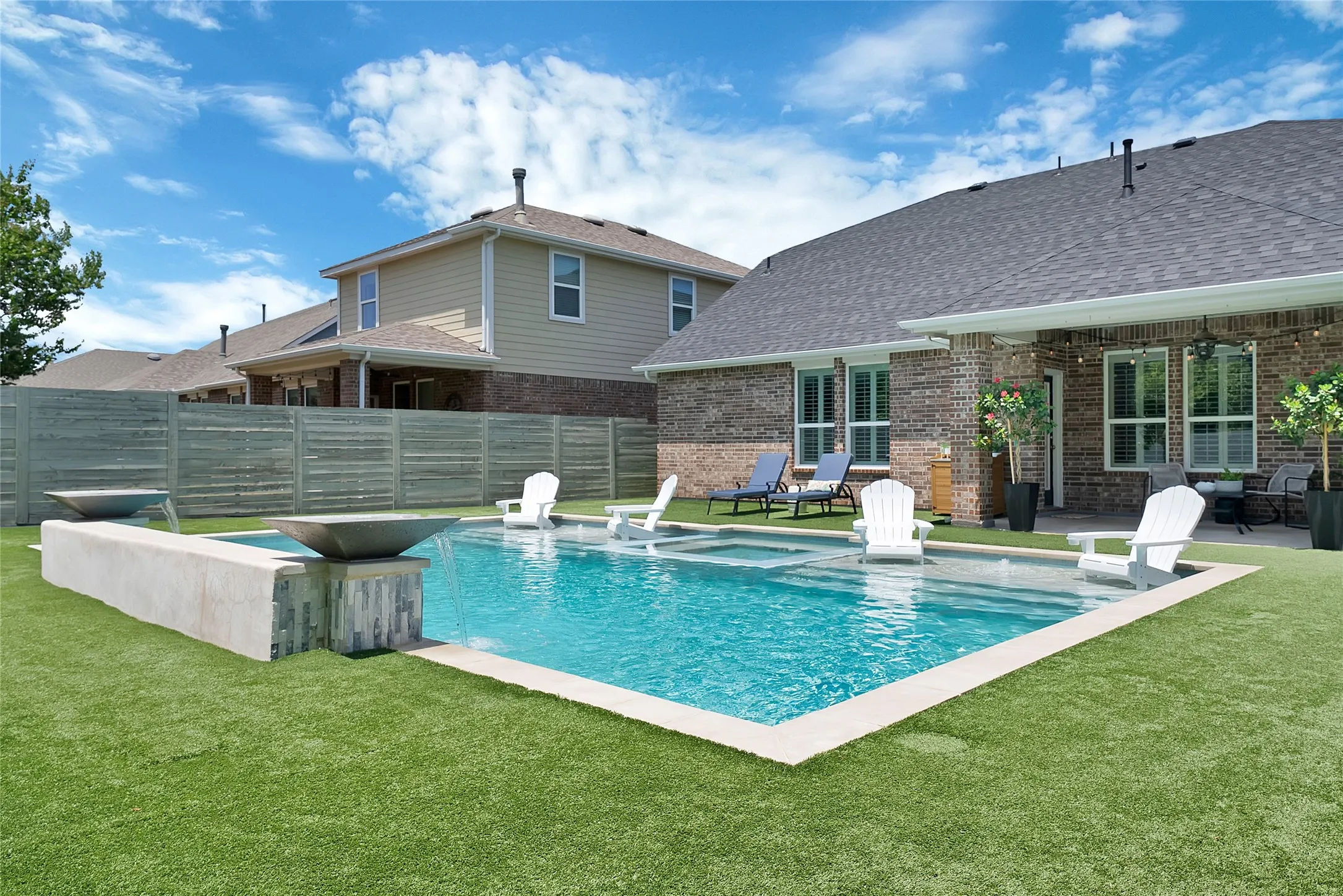 Backyard oasis featuring a swimming pool with integrated spa, waterfall feature, and artificial turf