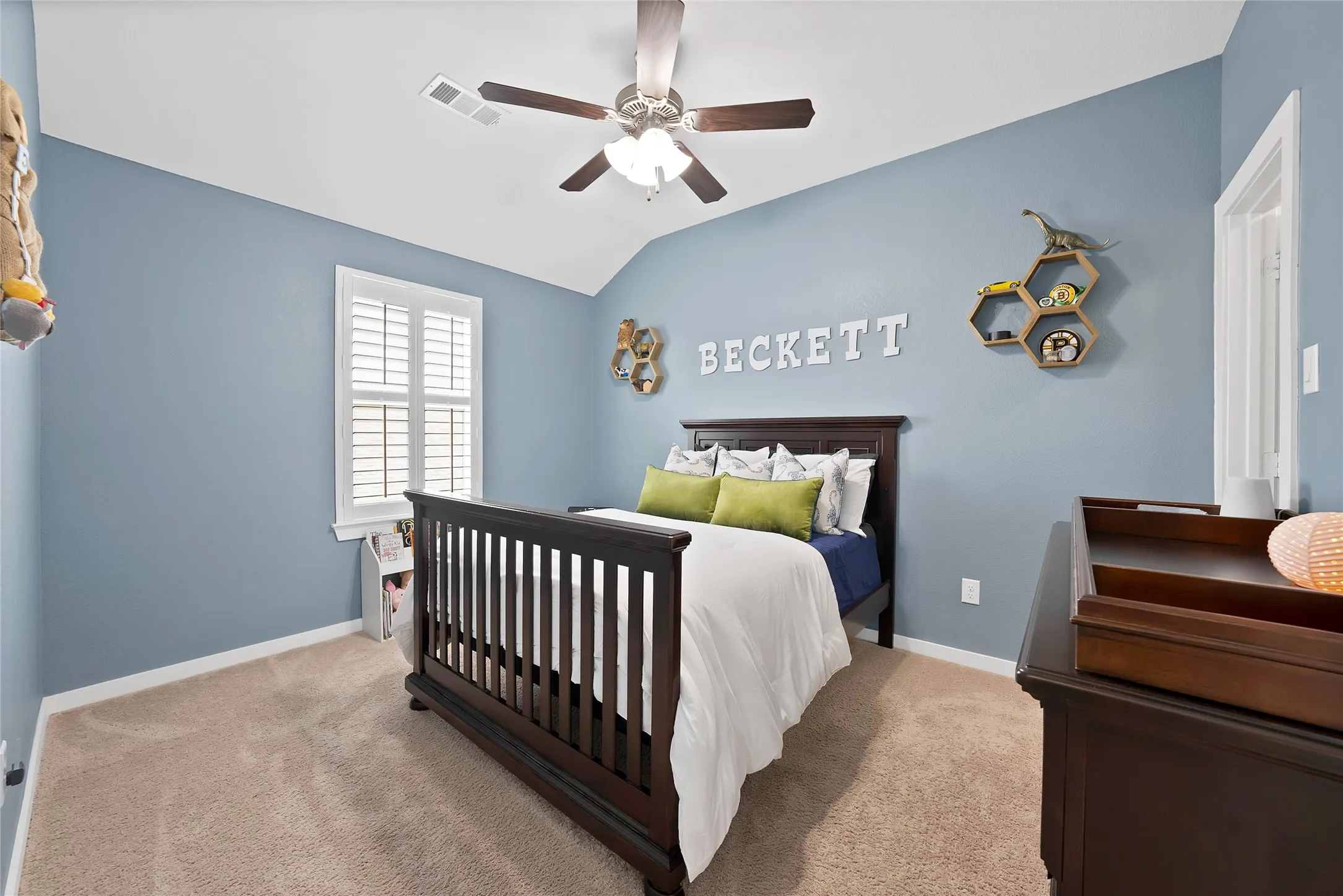 Carpeted room featuring a vaulted ceiling with a ceiling fan, a window with white louvered shutters, and light blue walls