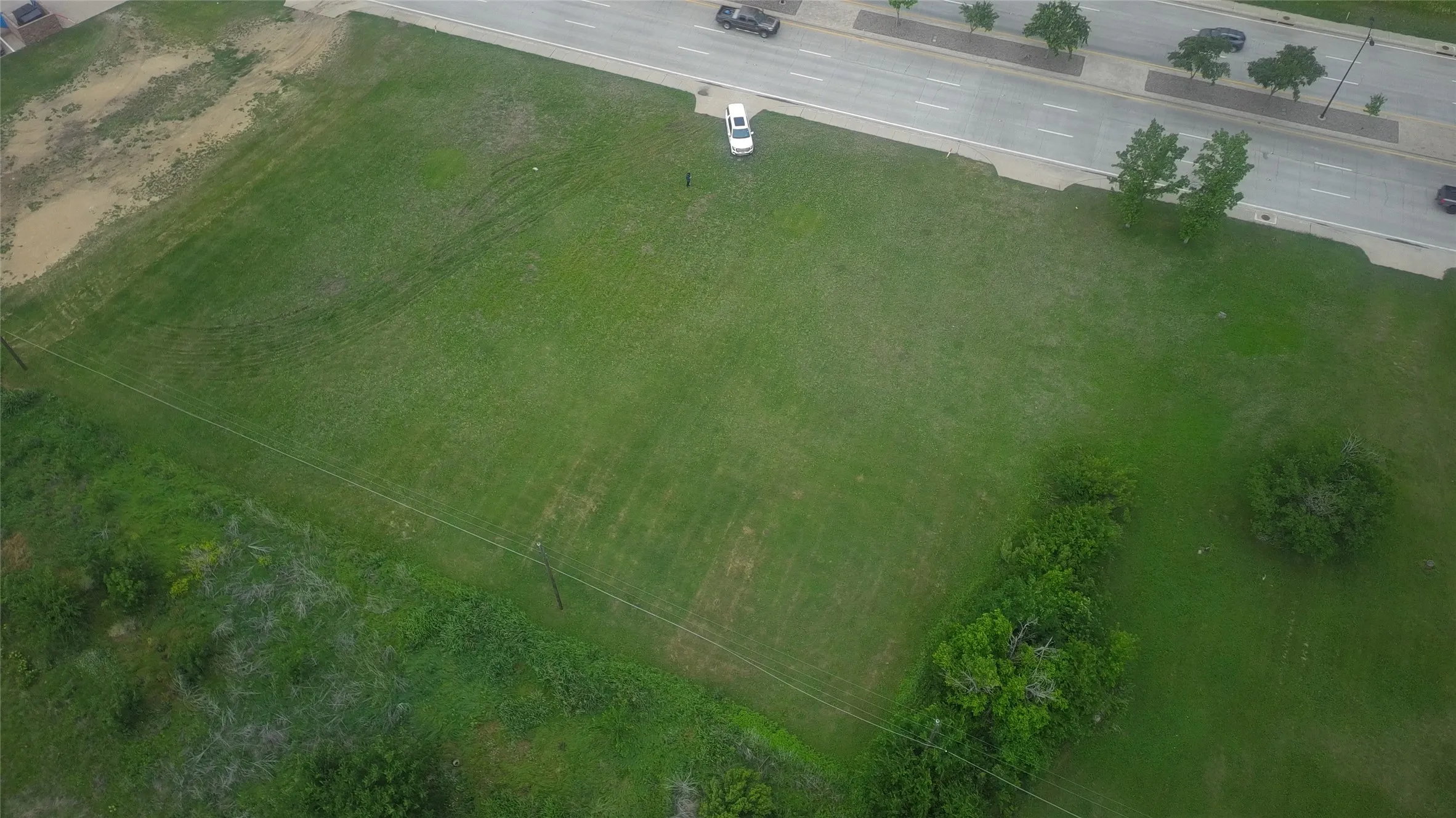 Expansive green lot featuring a paved roadway, mature trees, and overhead utility lines