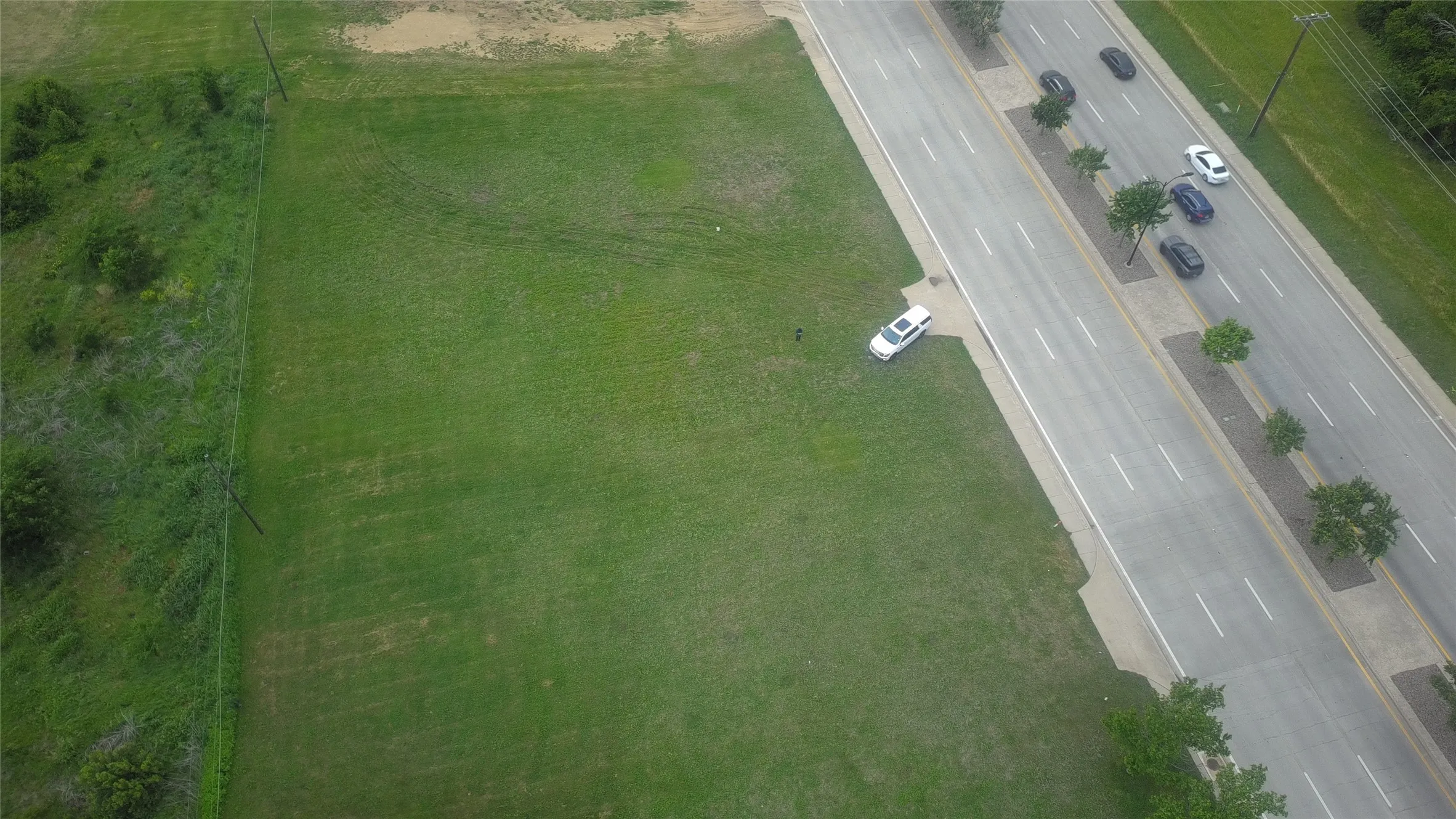 Expansive grassy lot bordered by a paved multi-lane road with a tree-lined median