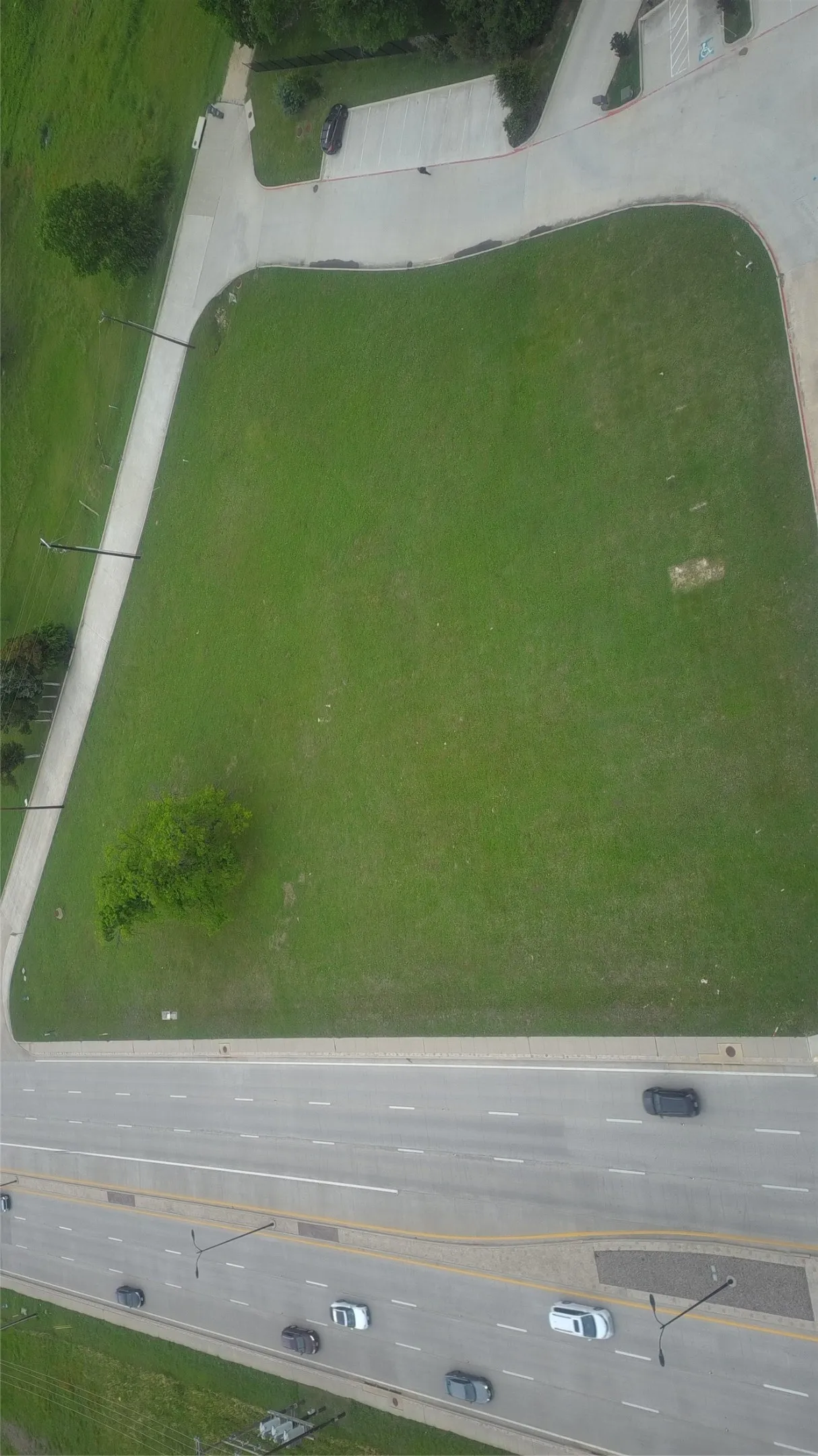 Expansive green lot featuring a mature tree, bordered by a multi-lane roadway and paved access ways