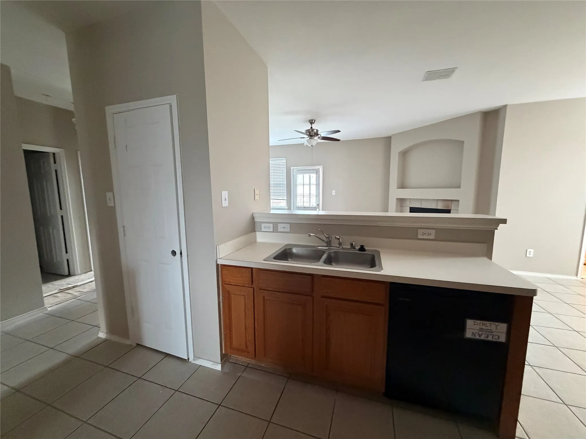 Kitchen with wood cabinetry, a double basin sink, and a dishwasher, featuring light-toned countertops