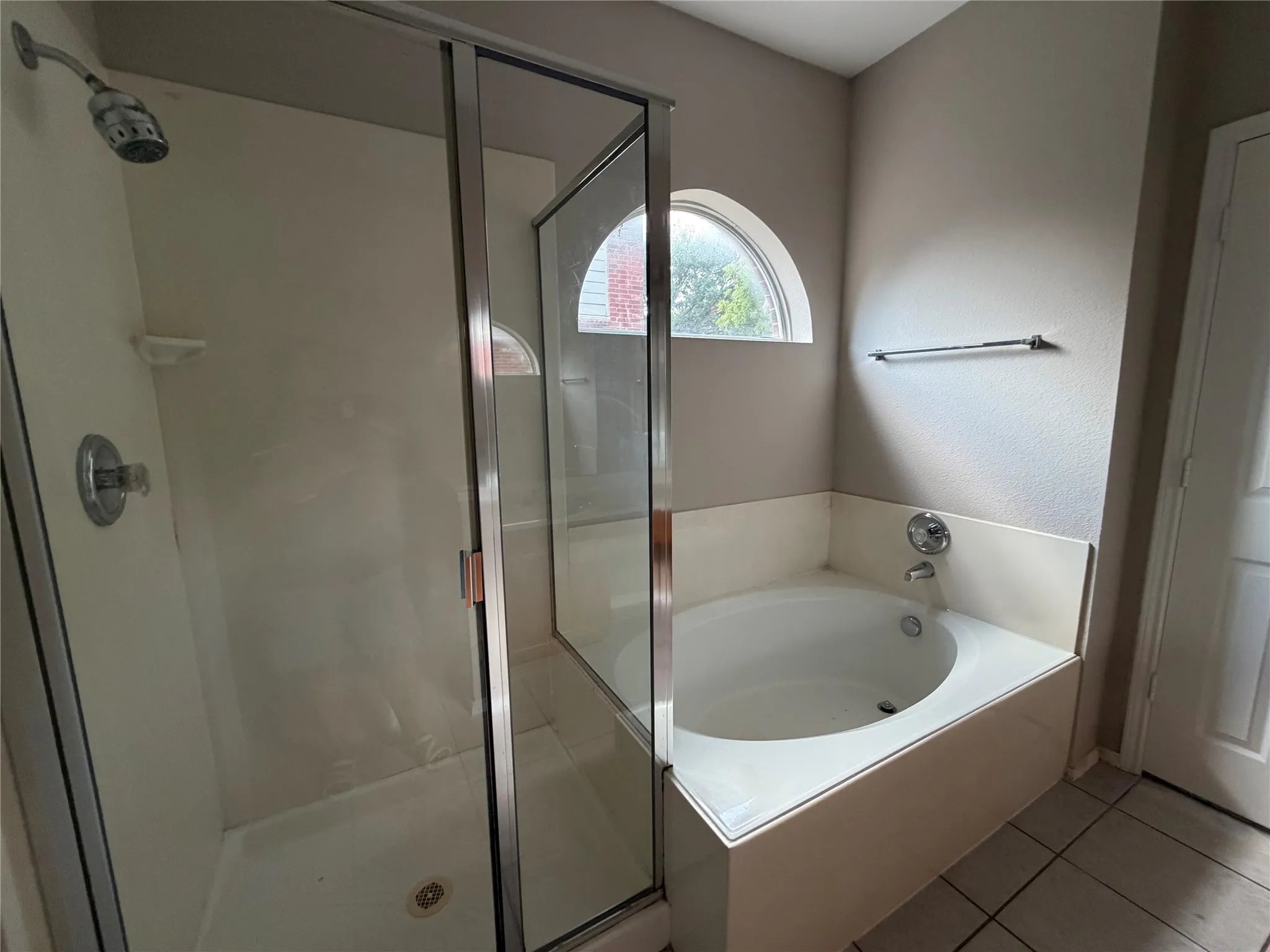 Walk-in shower with sliding glass door, built-in soaking tub, and arched window