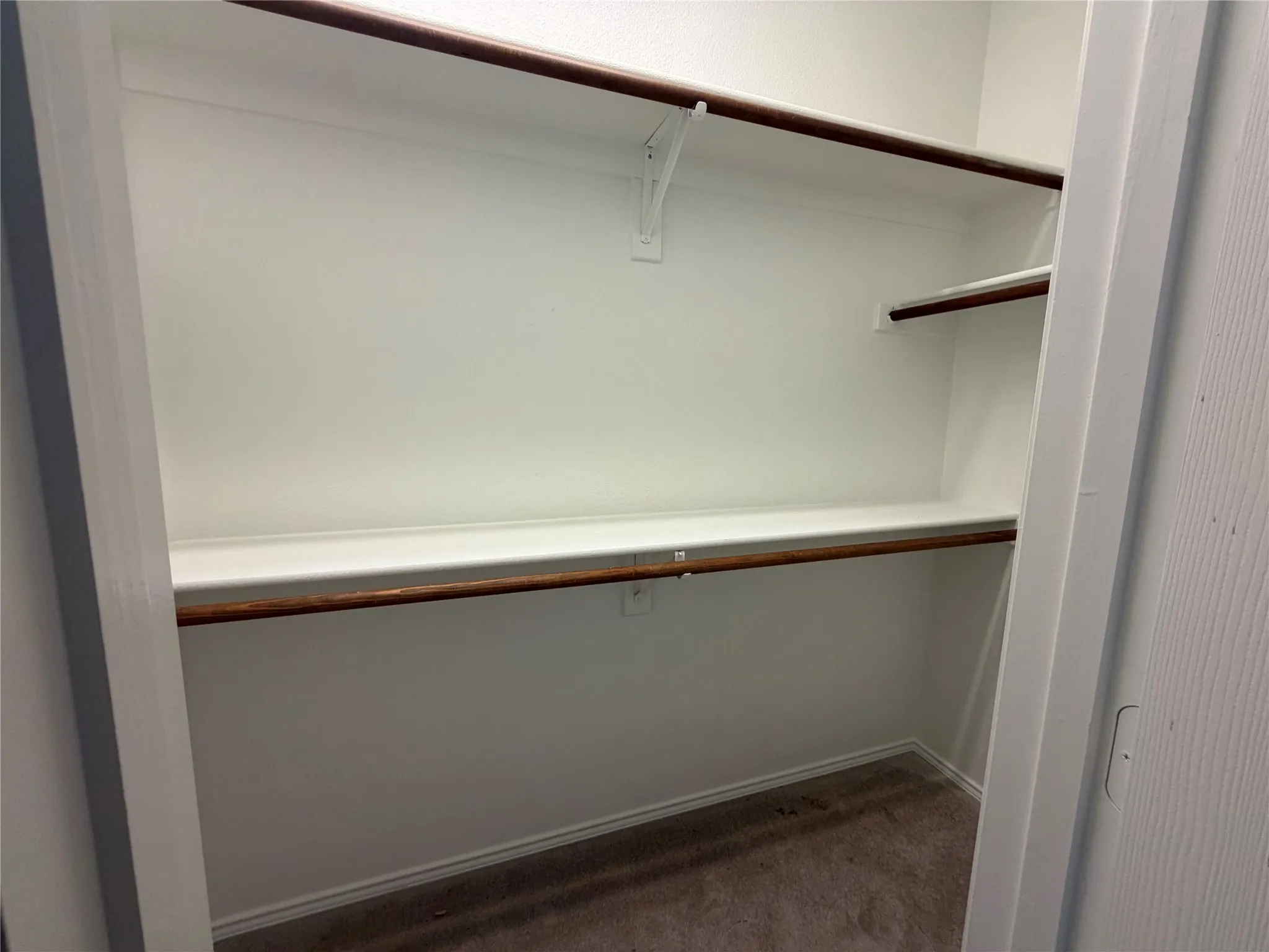 Built-in closet shelving with multiple hanging rods and a neutral carpeted floor