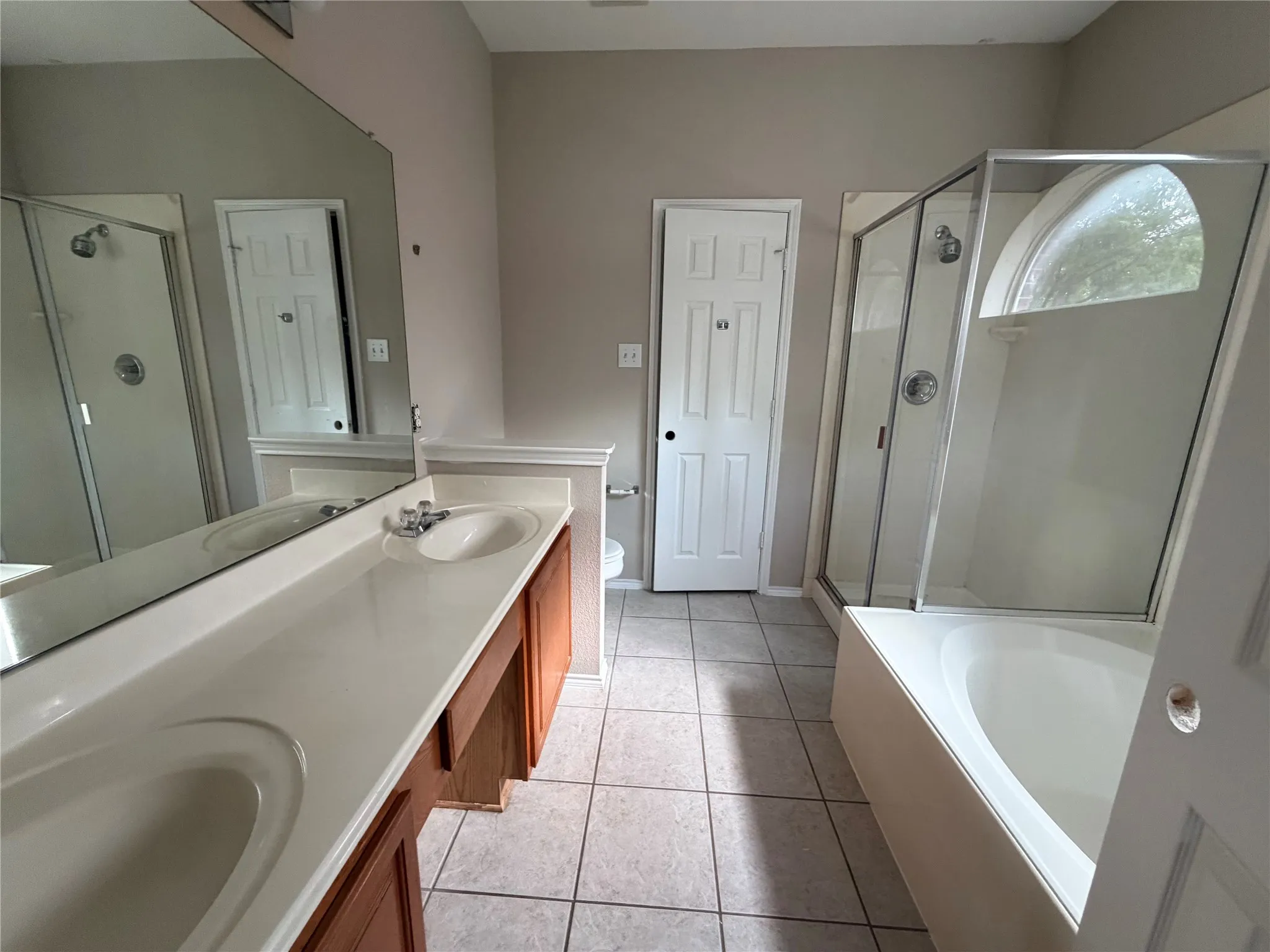 Primary bathroom featuring dual vanities with wood-finish cabinetry, ceramic tile flooring, and large framed mirrors