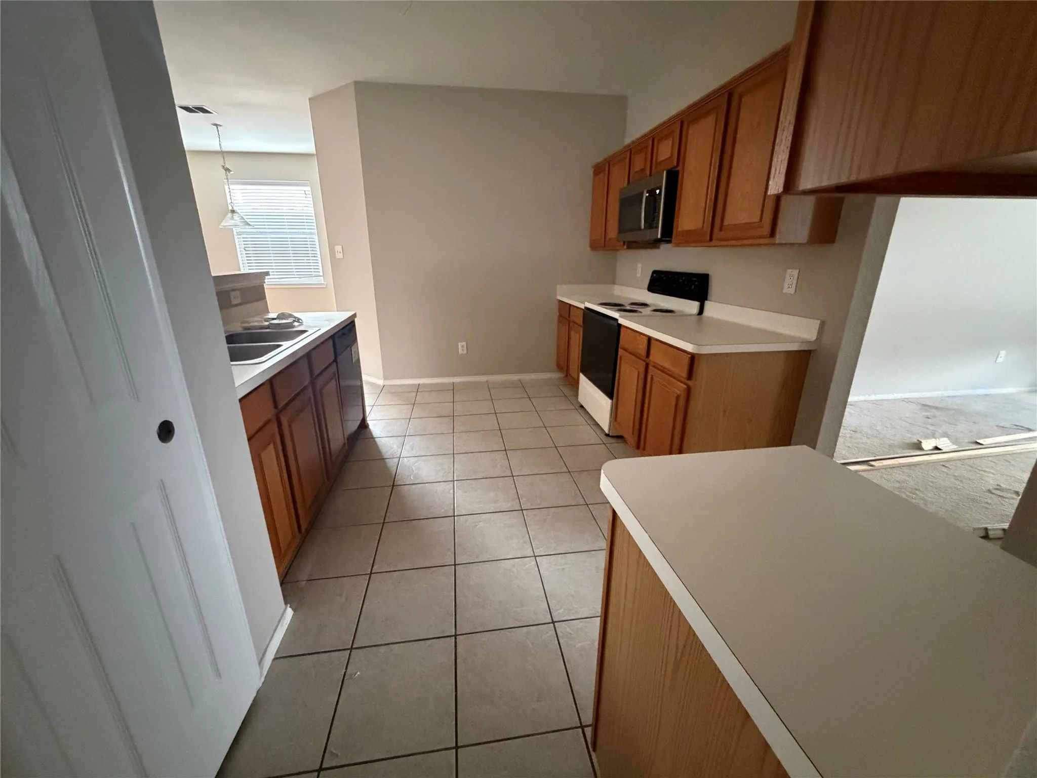 Kitchen featuring wood-finish cabinetry, light countertops, integrated stainless steel microwave, black electric range, and tile flooring