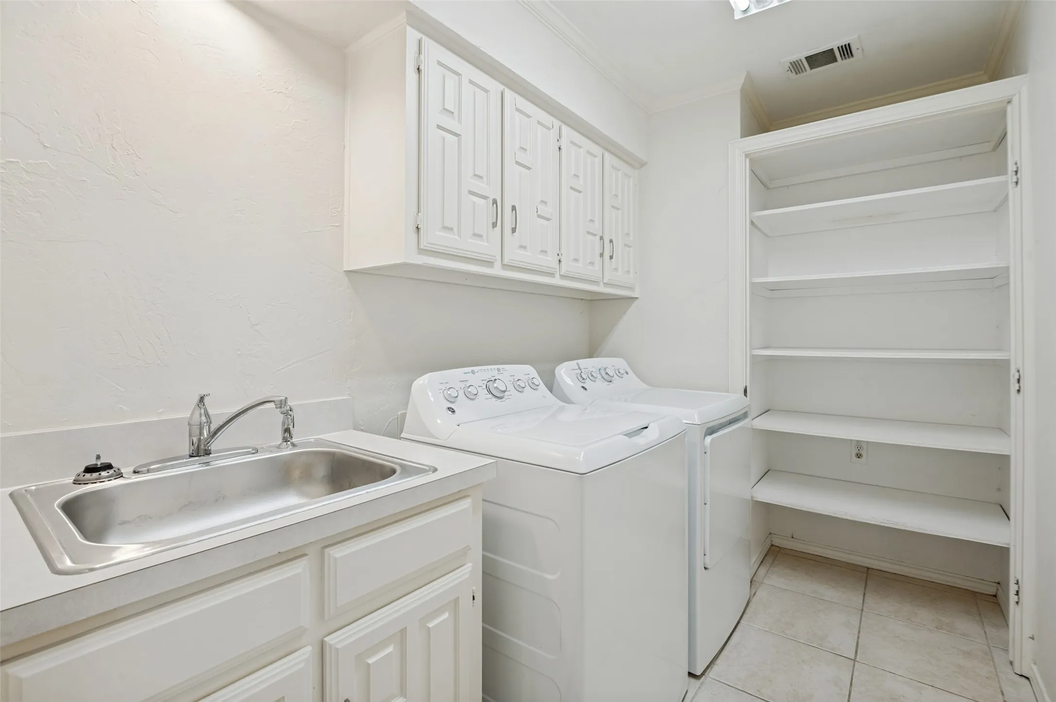 Full size laundry space with sink, built in cabinets and shelves, and access to a large storage area under the stairs.