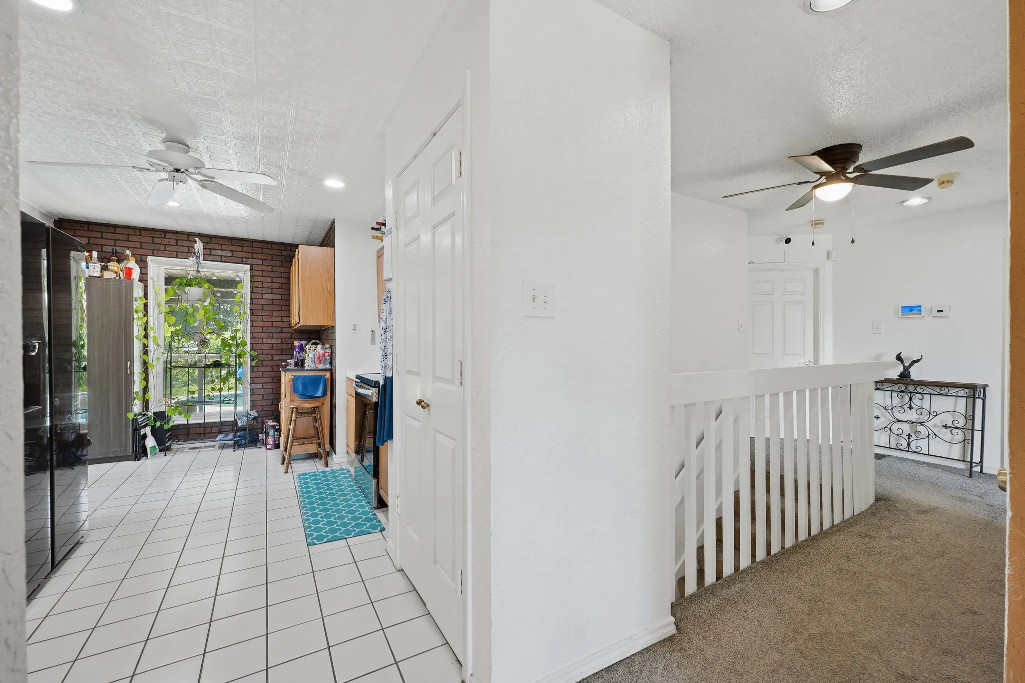 White tile flooring in the kitchen area featuring a brick accent wall and a window with a black railing