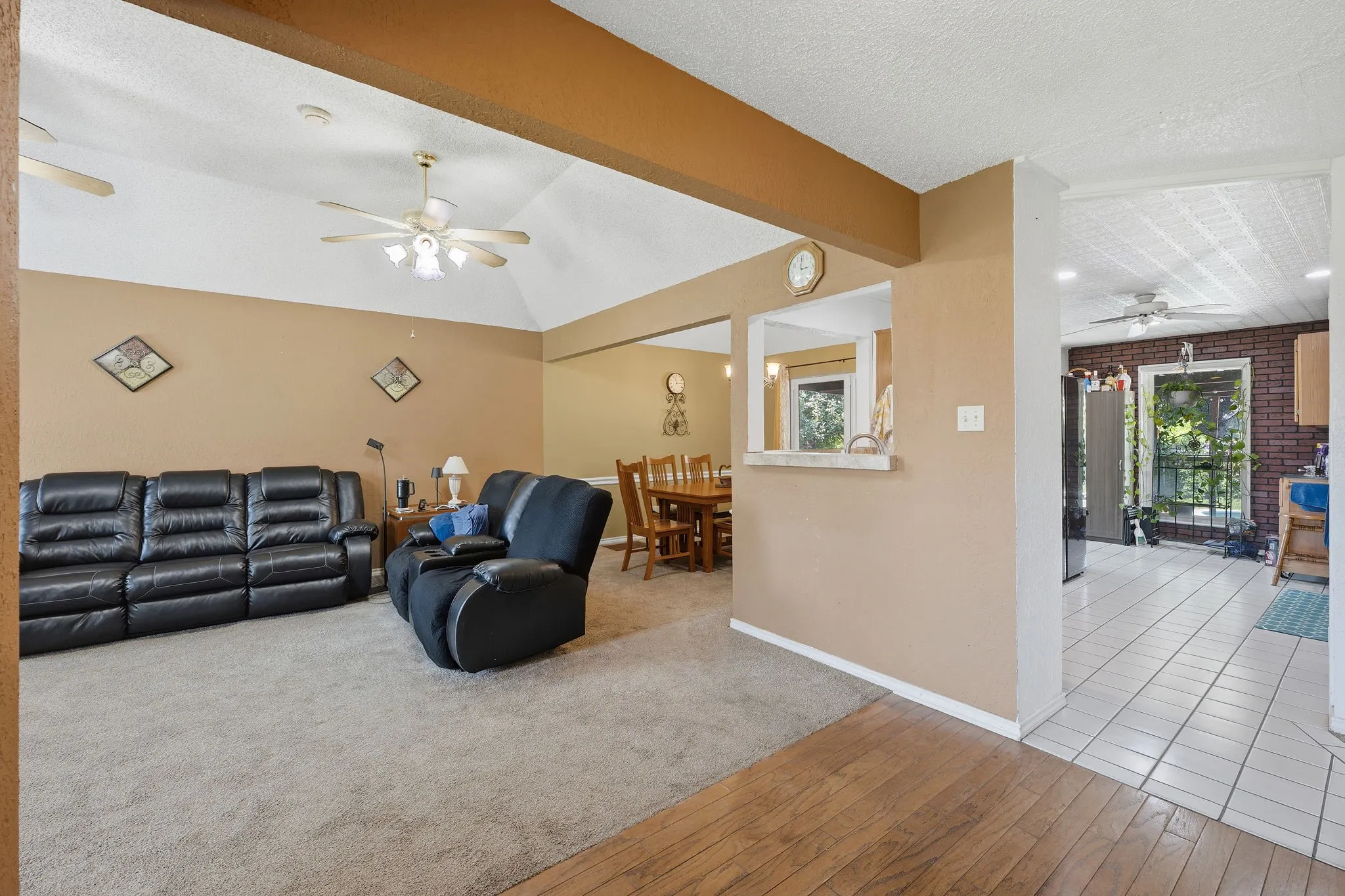 Vaulted ceiling living area with a ceiling fan, carpet flooring, and a pass-through window to the dining area
