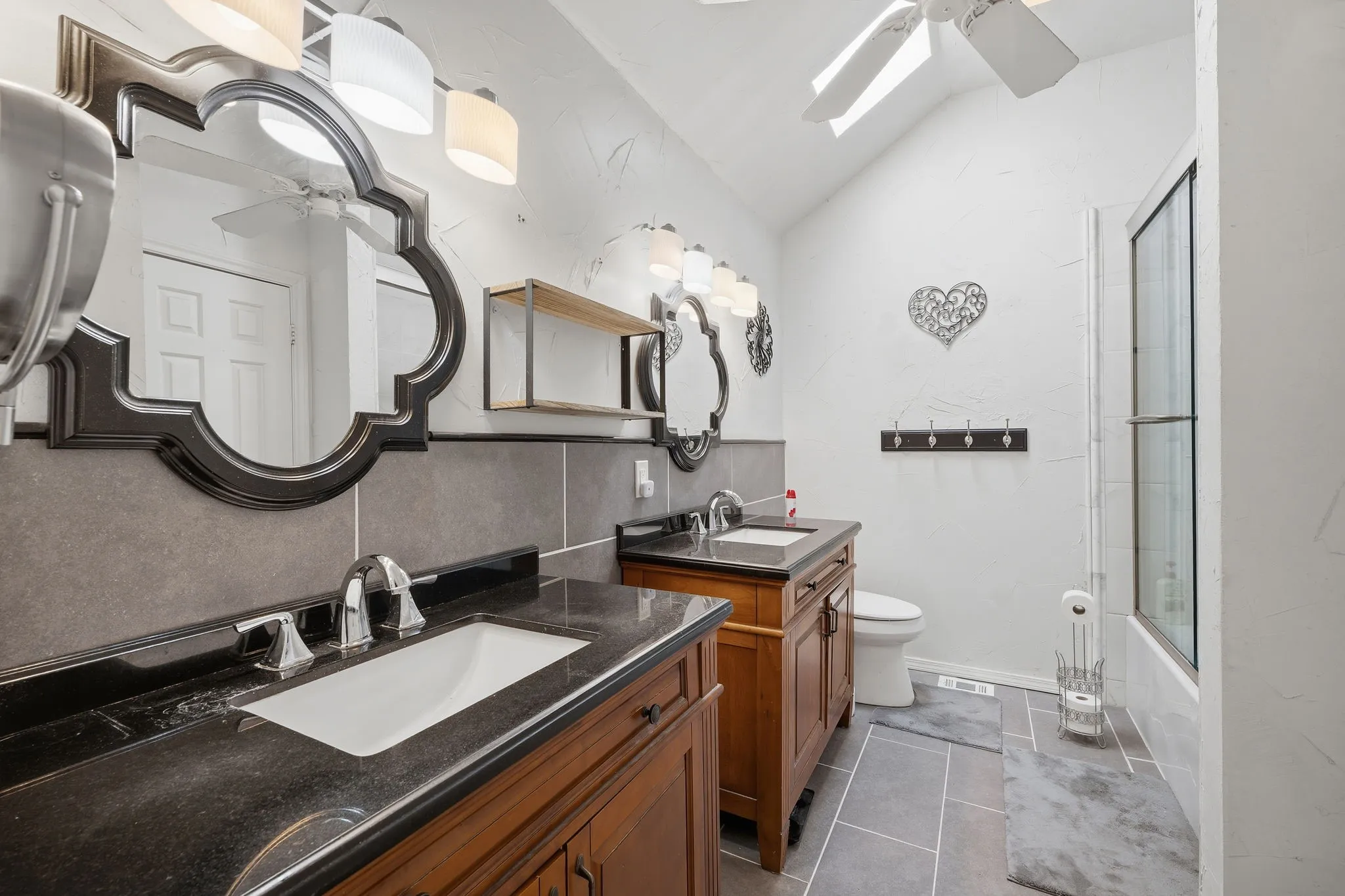 Spacious bathroom featuring dual wood-finish vanities with dark countertops and integrated sinks