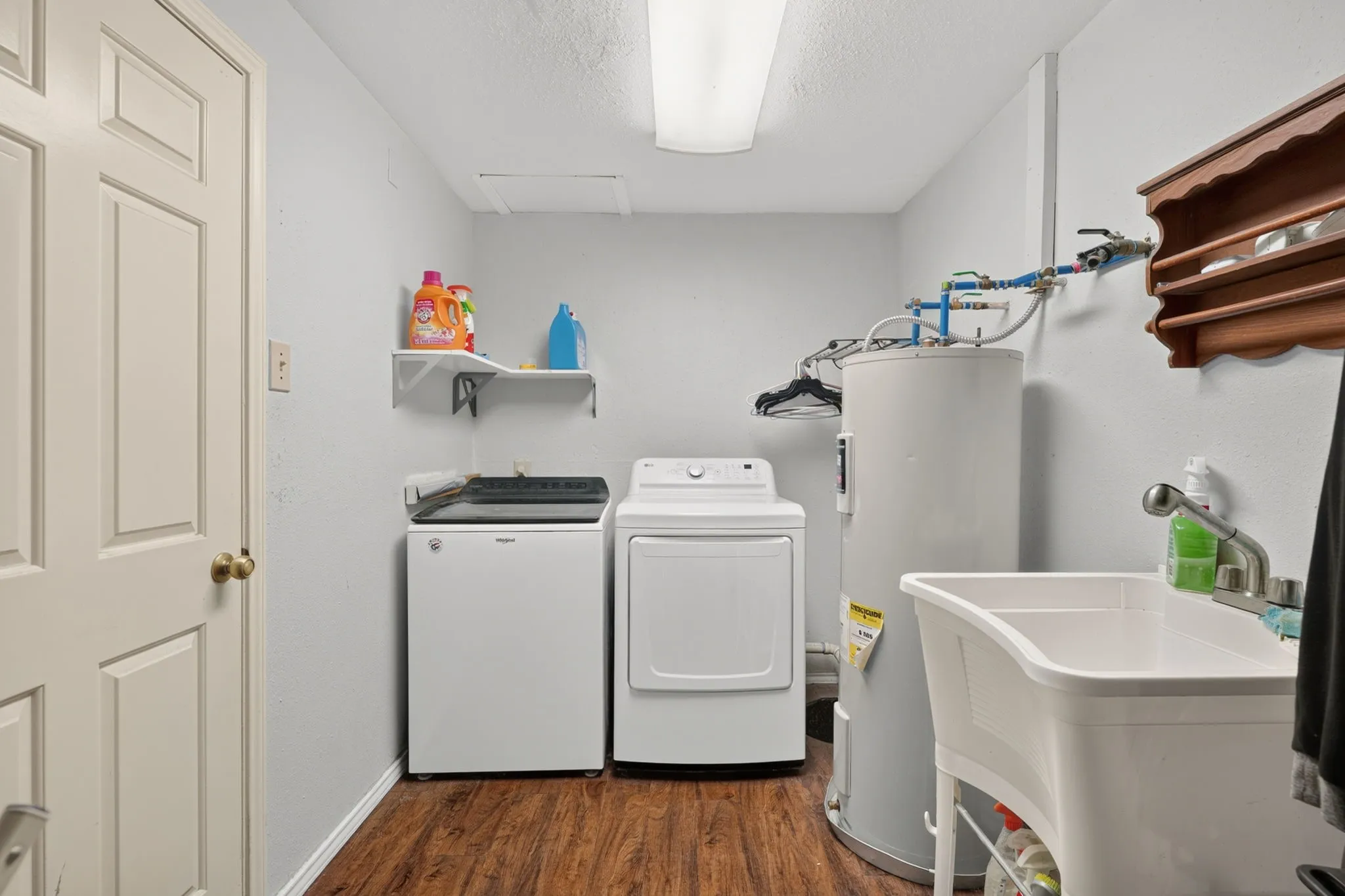 Dedicated utility space featuring wood-finish flooring, a white utility sink with a chrome faucet, and overhead fluorescent lighting