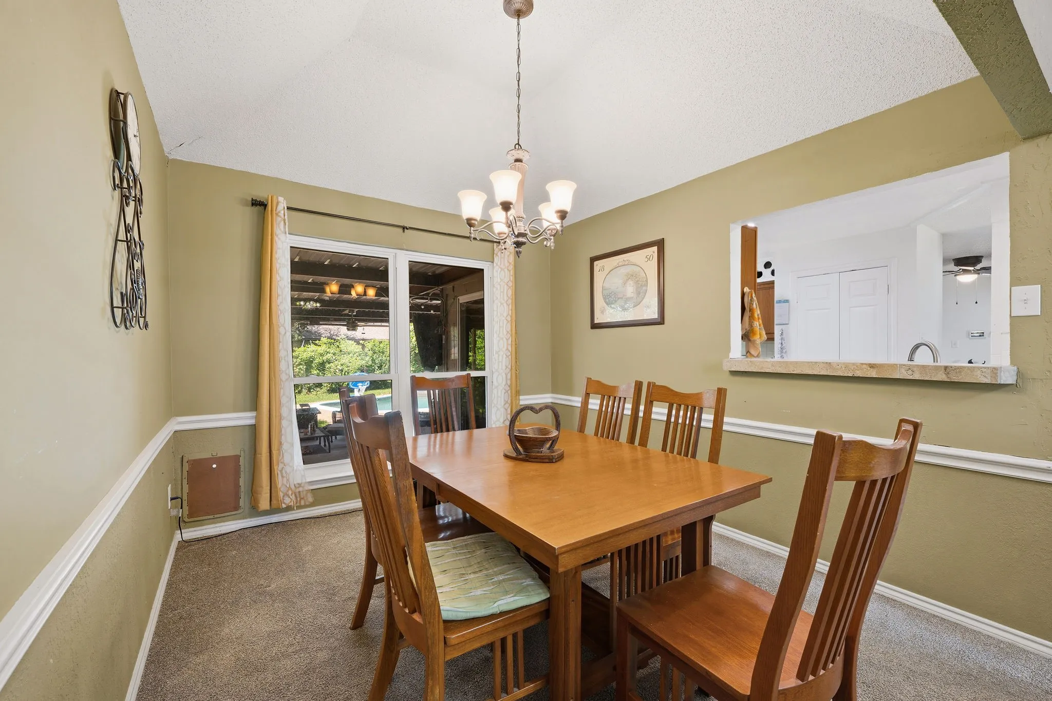 Dining area featuring a vaulted ceiling with a chandelier, two-tone painted walls with chair rail molding, and a pass-through window to an adjacent room