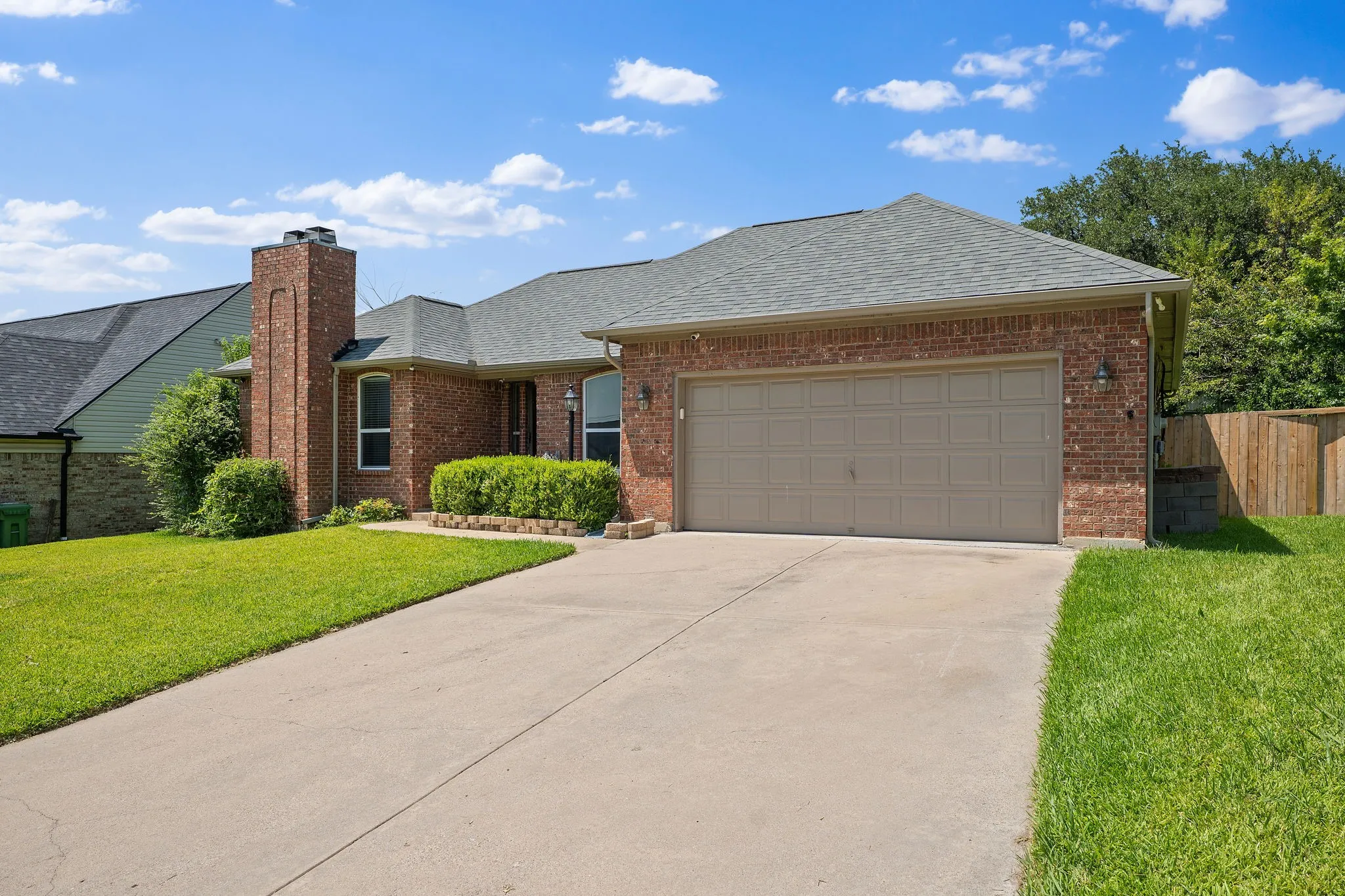 Brick exterior residence featuring a two-car garage with a tan door, a chimney, and a concrete driveway