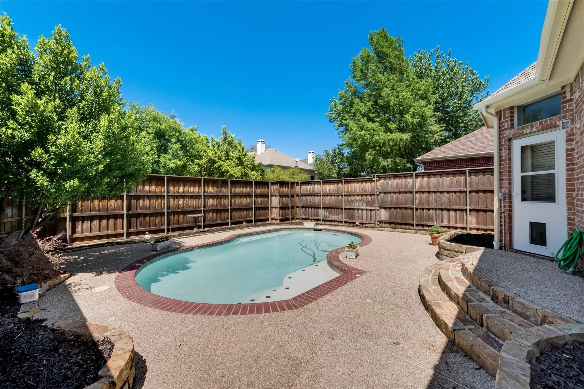 Kidney-shaped swimming pool with brick coping, surrounded by an exposed aggregate patio