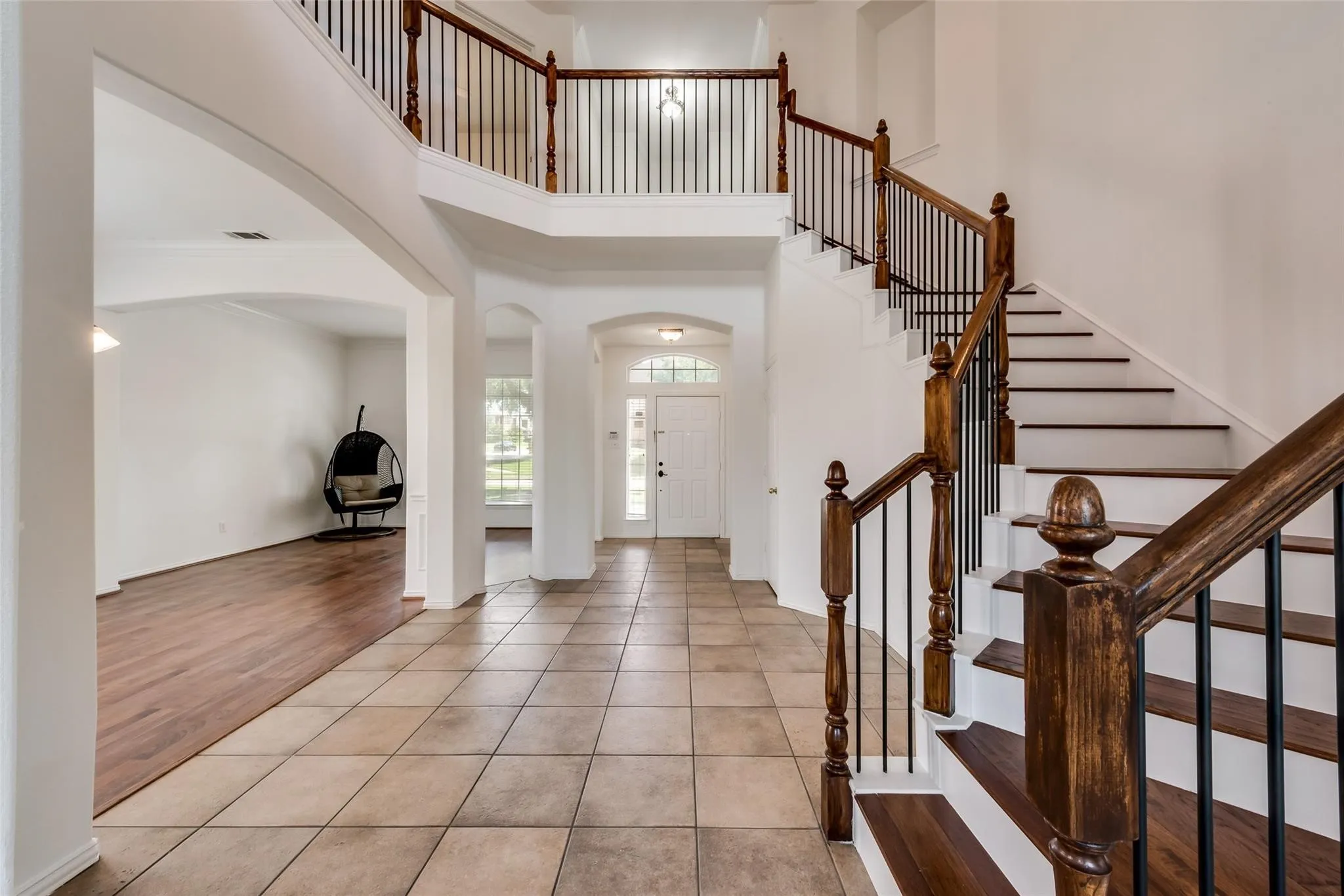 Two-story foyer featuring a grand staircase with wood newel posts and black iron balusters, tile flooring, and arched doorways