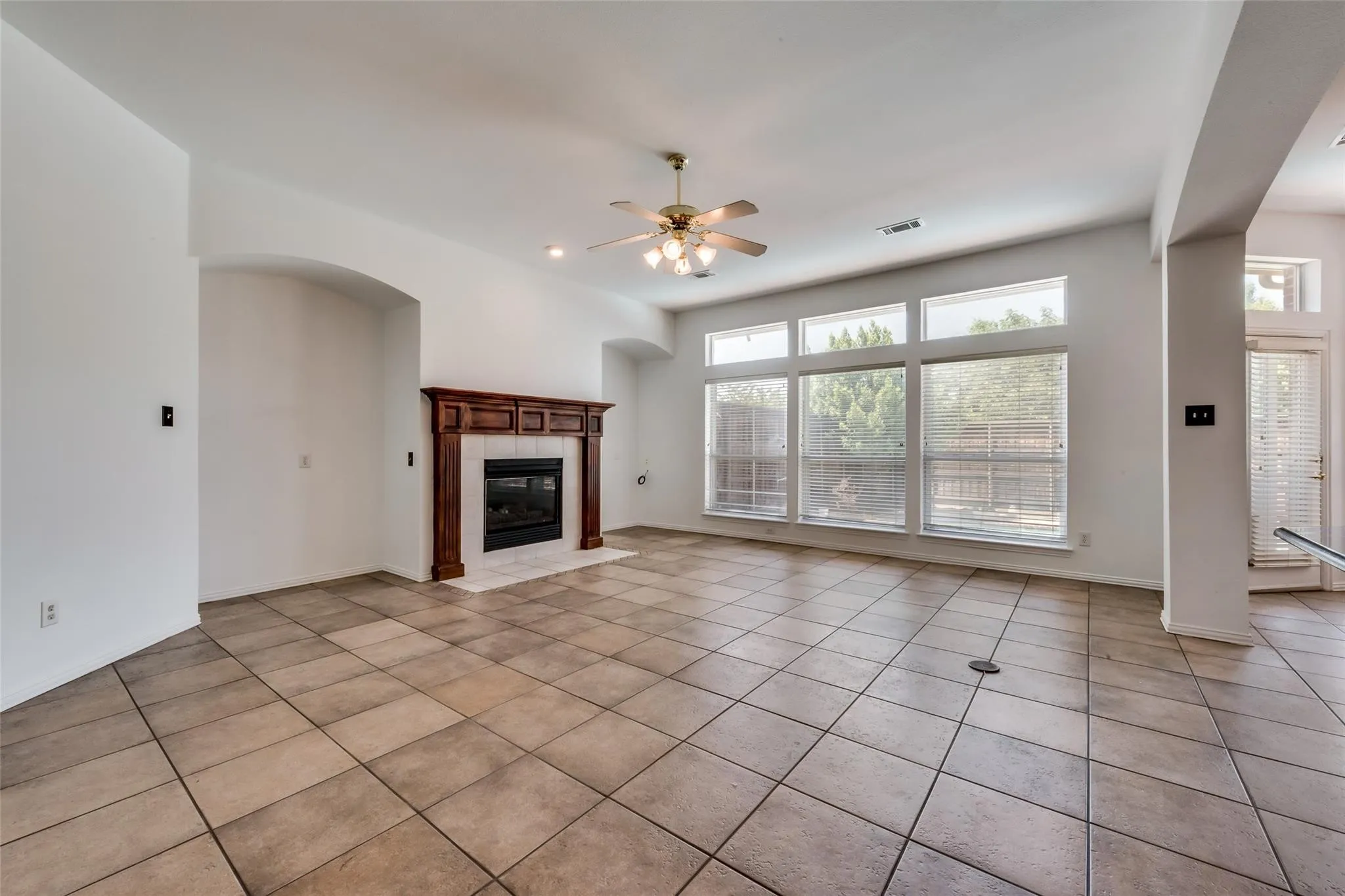 Spacious living area featuring large format tile flooring, a dark wood mantel fireplace with a tile surround, and expansive windows