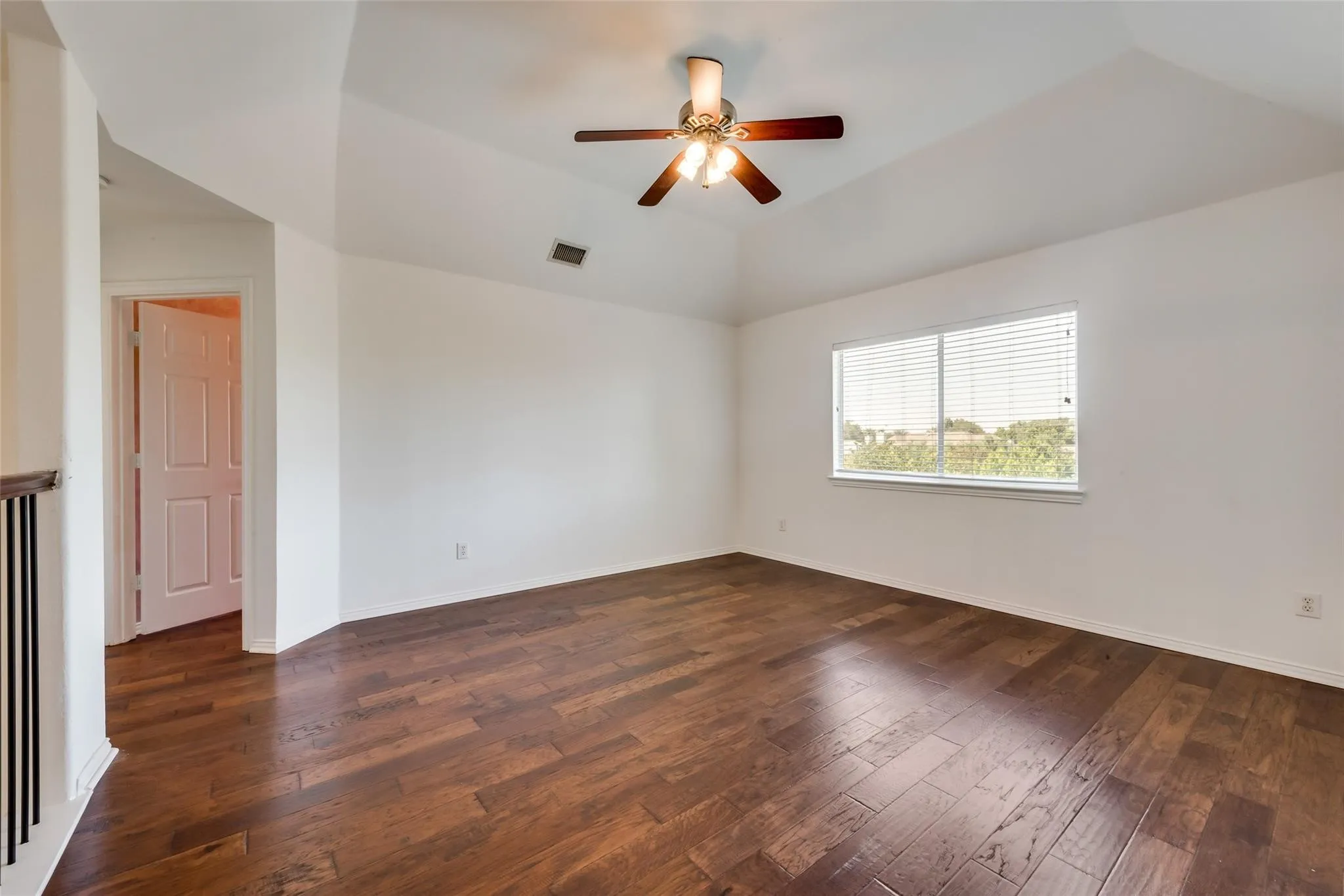 Spacious room featuring wood-finish flooring, a vaulted ceiling, and a ceiling fan with light fixture