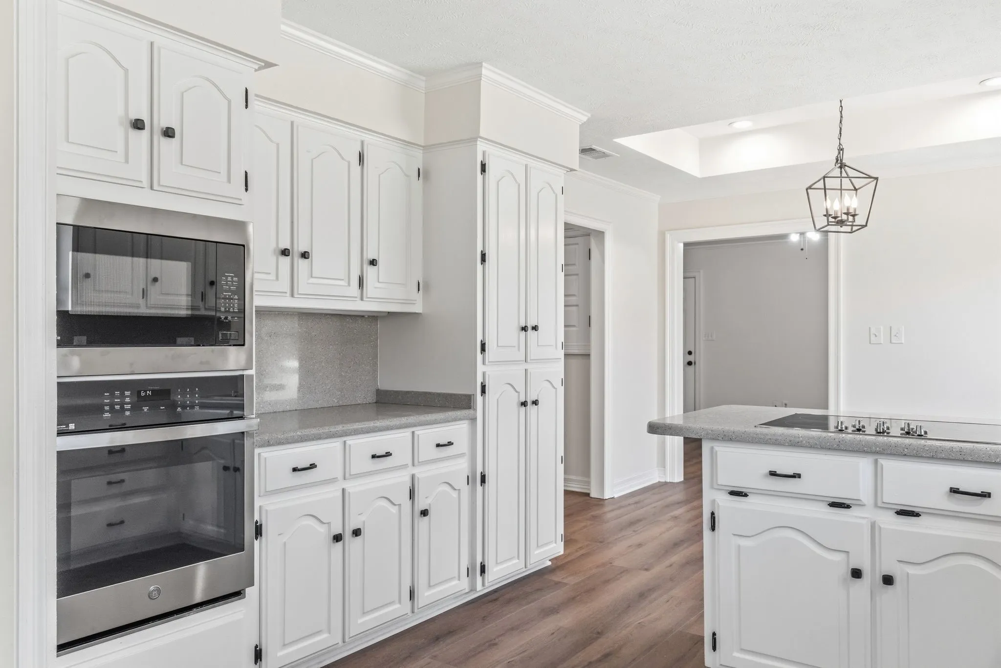 Kitchen featuring white cabinetry with black hardware, built-in stainless steel appliances, speckled countertops, and wood-finish flooring