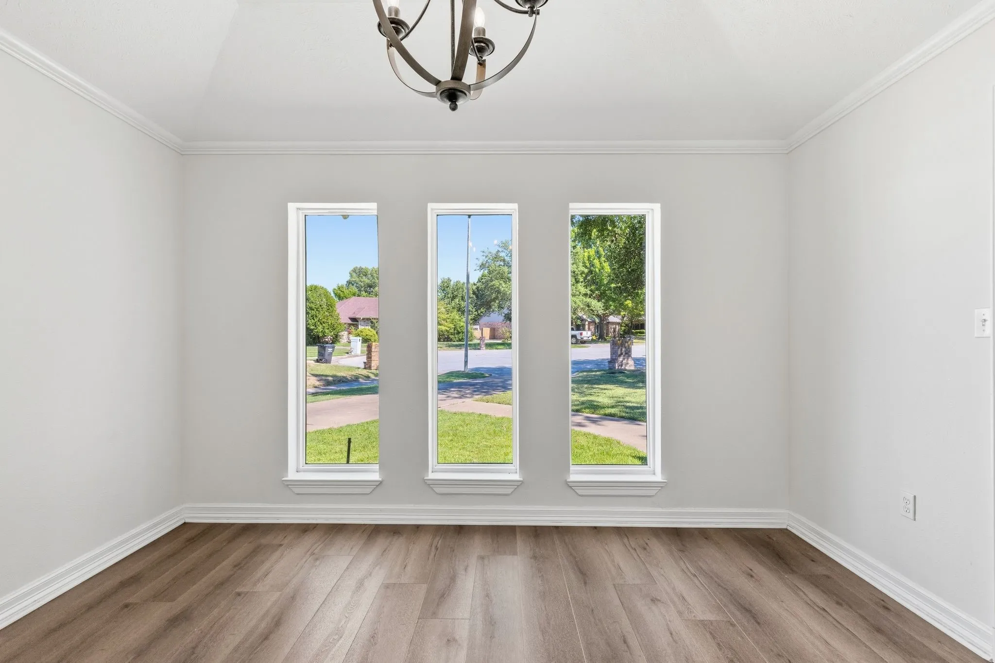 Interior space featuring three rectangular windows, wood-finish flooring, light gray walls, white trim, and a vaulted ceiling with a circular chandelier