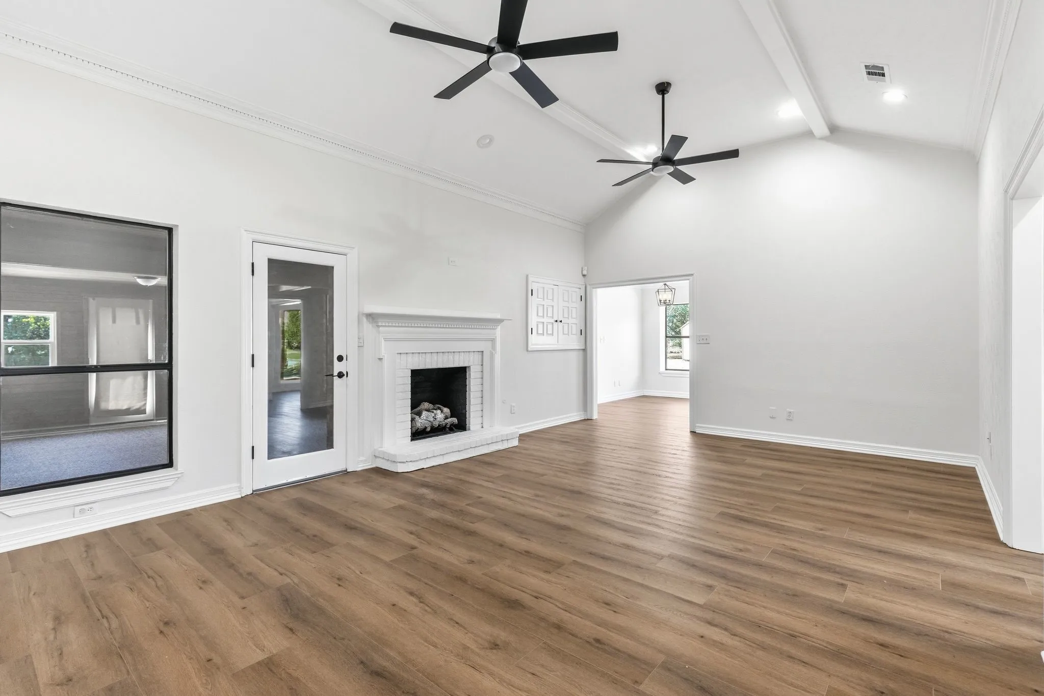 Spacious living area featuring wood-finish flooring, a white brick fireplace with mantel, and a glass-paned door