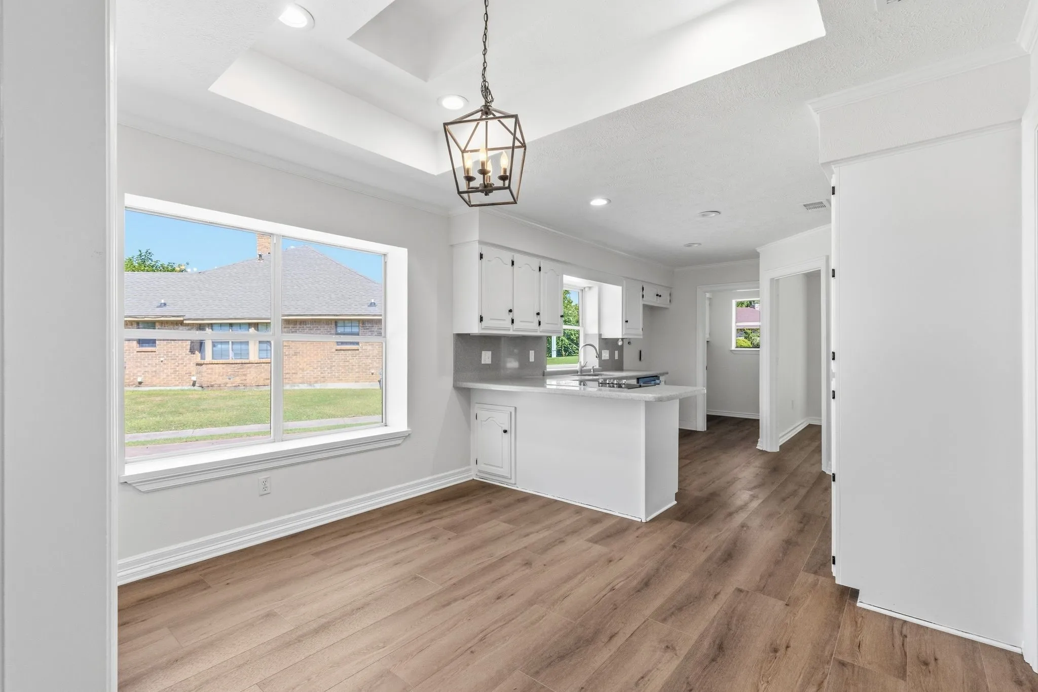 Spacious dining area featuring wood-finish flooring, a large window, and a tray ceiling with a dark bronze chandelier