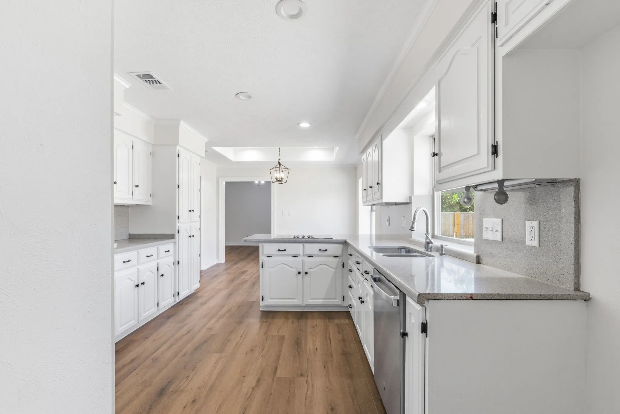 Spacious kitchen featuring white cabinetry, light-toned countertops, wood-finish flooring, and recessed lighting