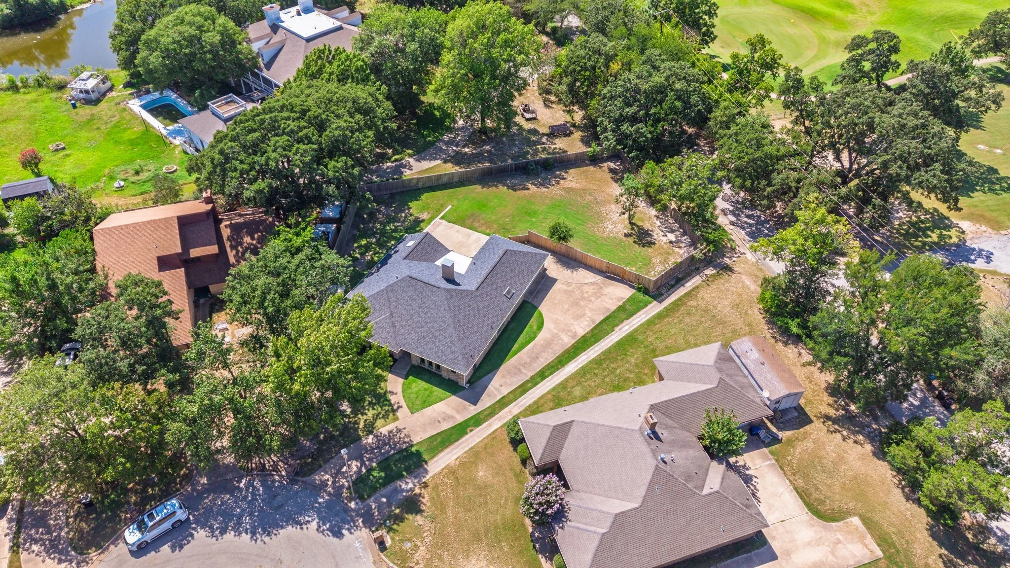 Aerial perspective showcasing a property with a dark shingle roof, a paved driveway, and a fenced backyard
