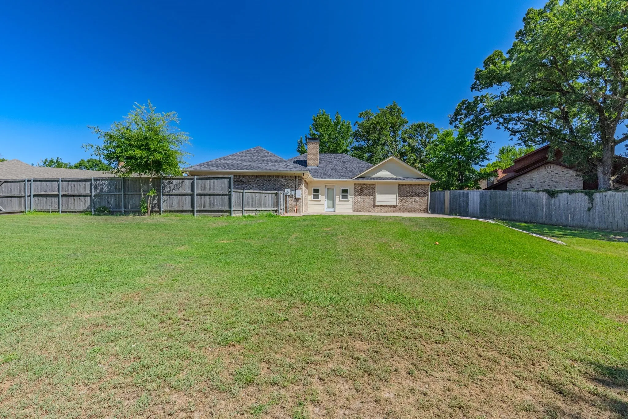 Expansive rear yard featuring a privacy fence, established trees, and a brick exterior