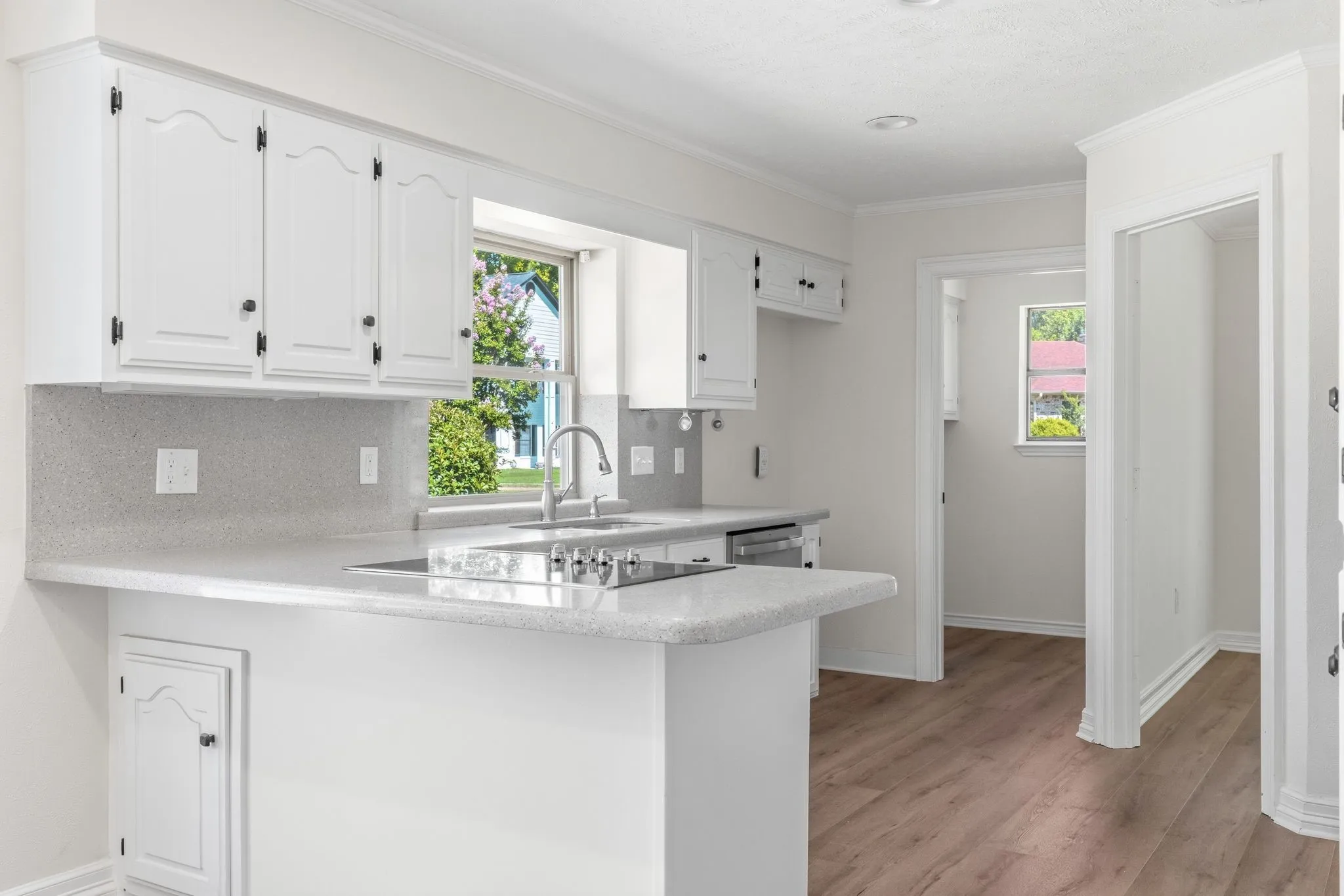 Kitchen featuring white cabinetry, light-toned countertops, a stainless steel sink with a gooseneck faucet, a built-in cooktop, and wood-finish flooring