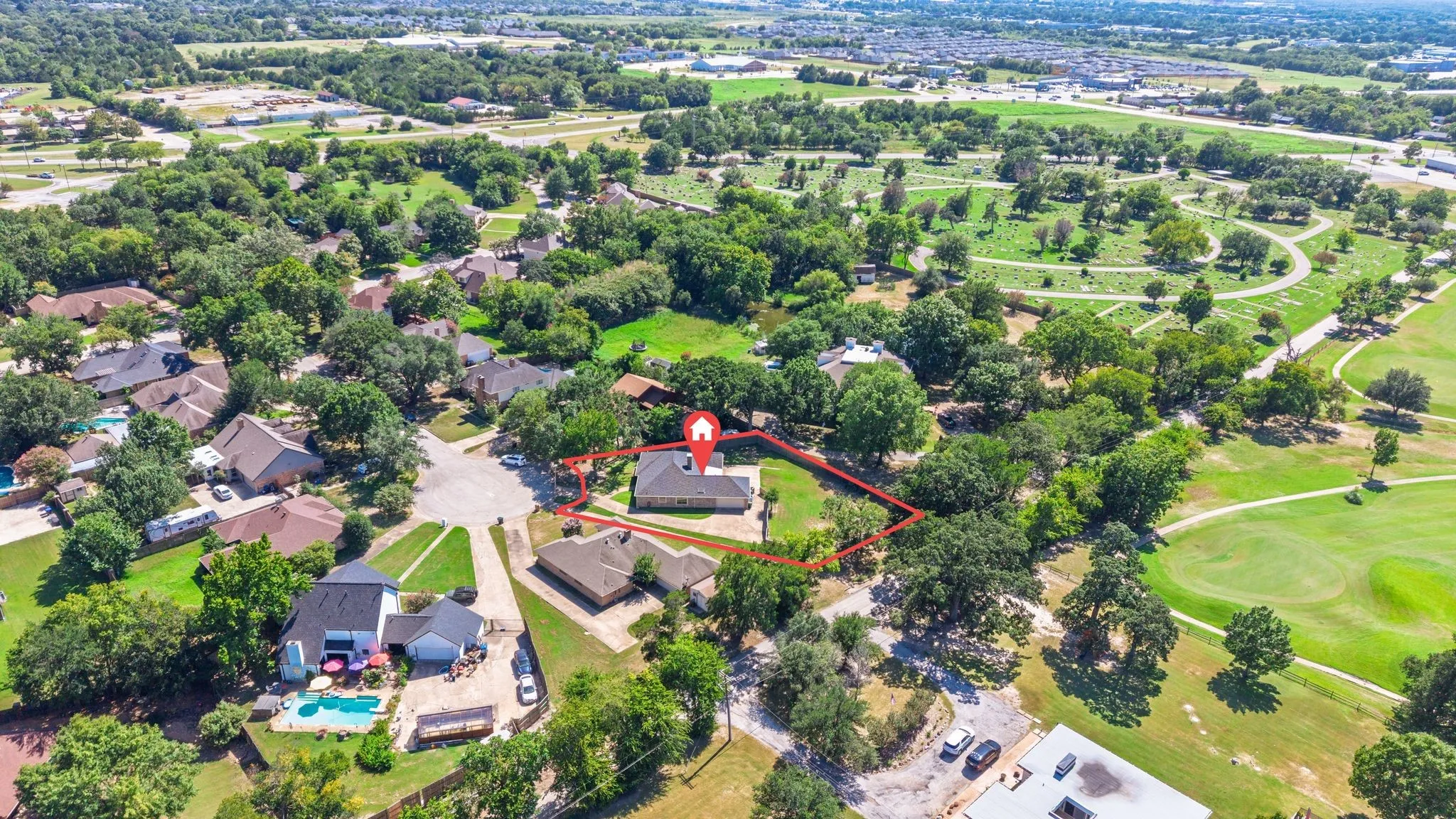Aerial perspective showcasing a single-story residence with a light-colored roof, surrounded by mature trees