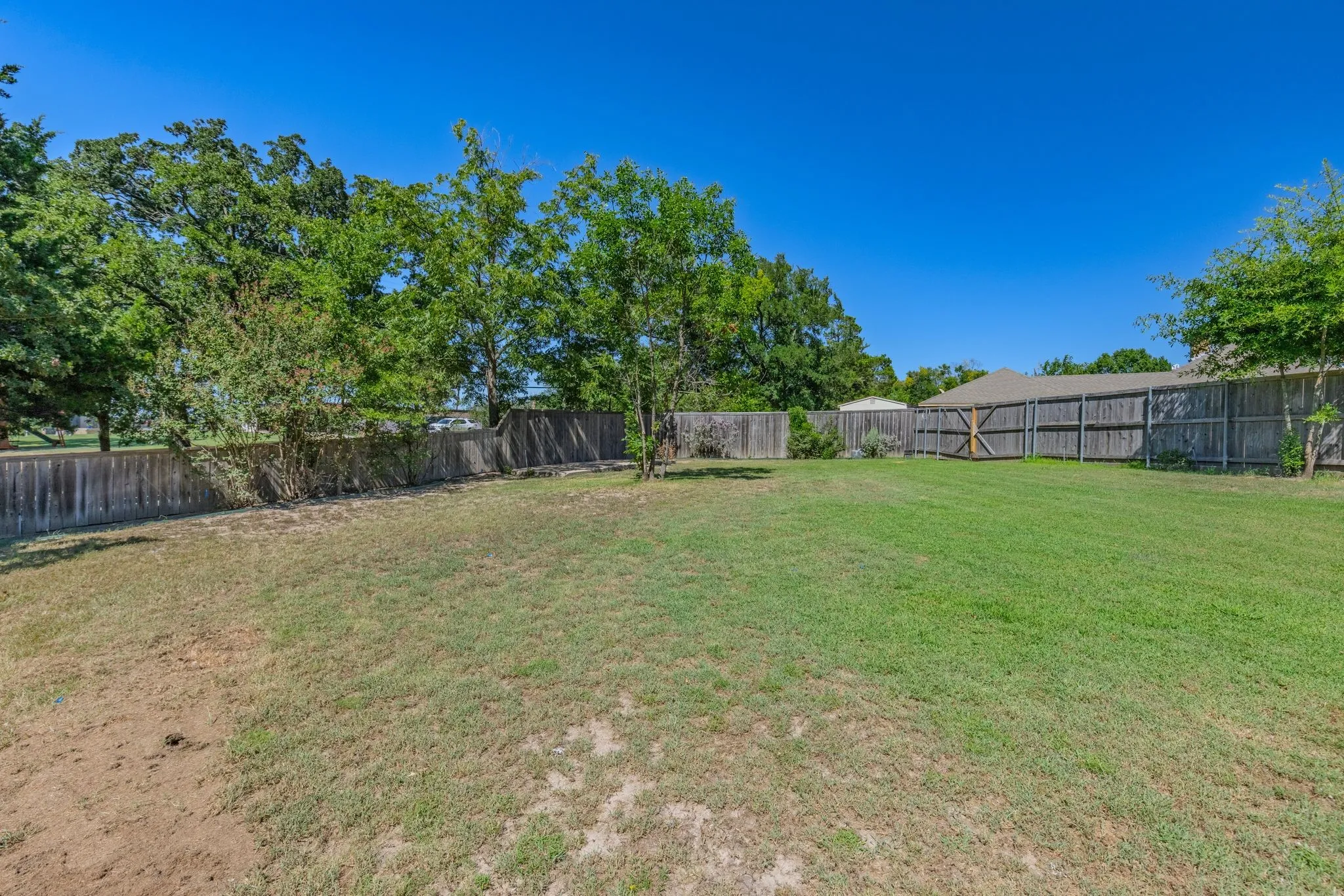 Expansive rear yard featuring a wood privacy fence, mature trees, and a wooden gate