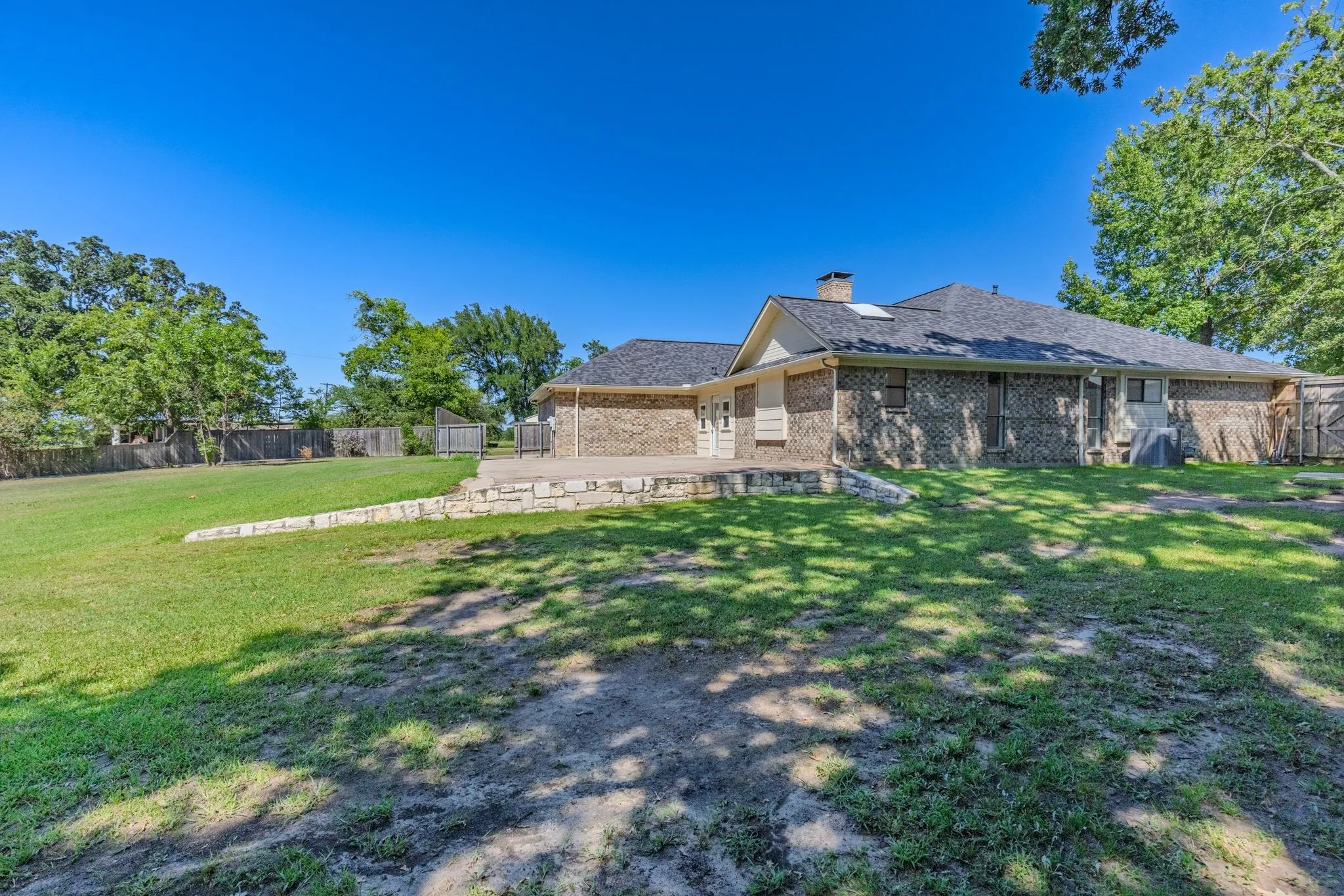 Expansive green space featuring a brick exterior, a stone patio, and a shingled roof