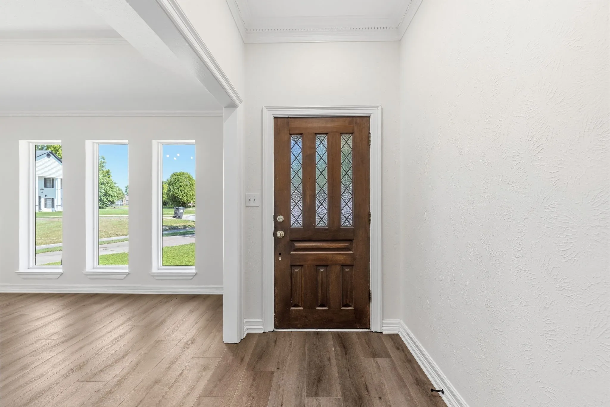 Entryway featuring a paneled wood-finish door with decorative glass inserts, wood-finish flooring, white trim, and multiple vertical windows
