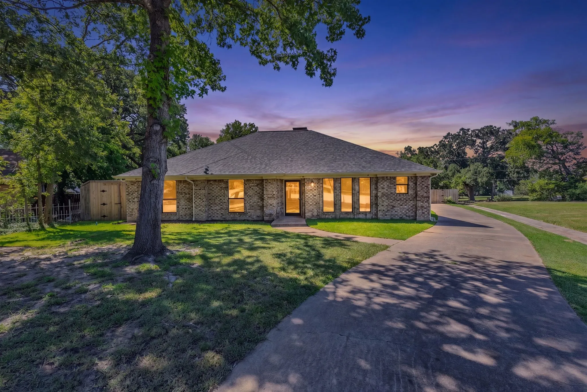 Brick exterior residence with a gray shingle roof and a lengthy concrete driveway