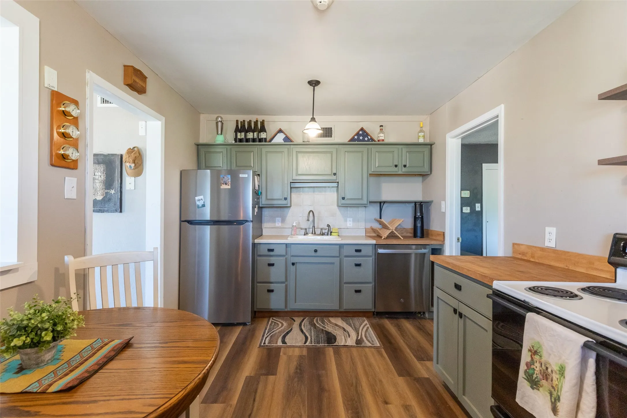 Kitchen featuring sage cabinetry, stainless steel appliances, wood-finish flooring, a tile backsplash, and butcher block countertops