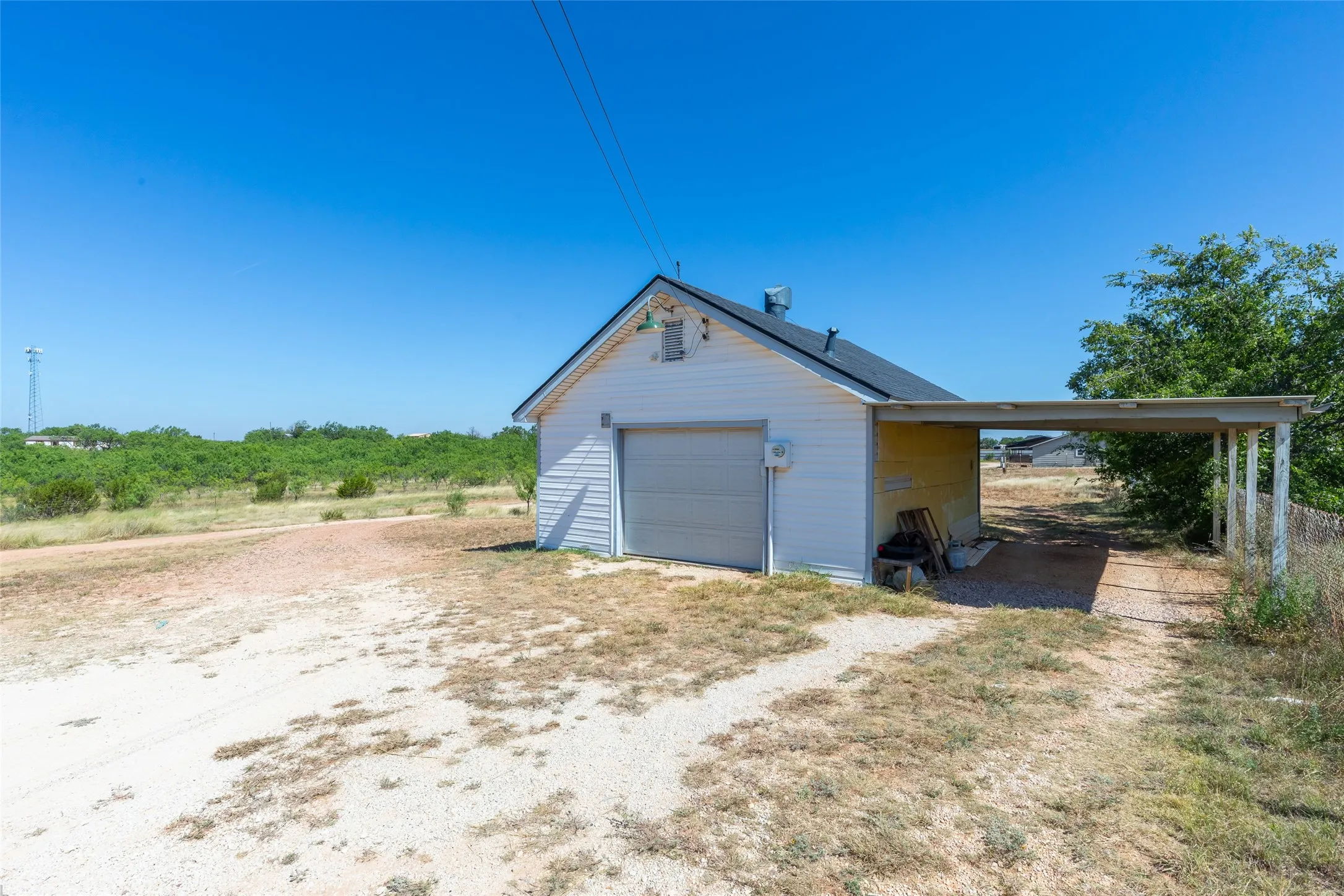 Detached garage with a roll-up door, white siding exterior, and an attached carport