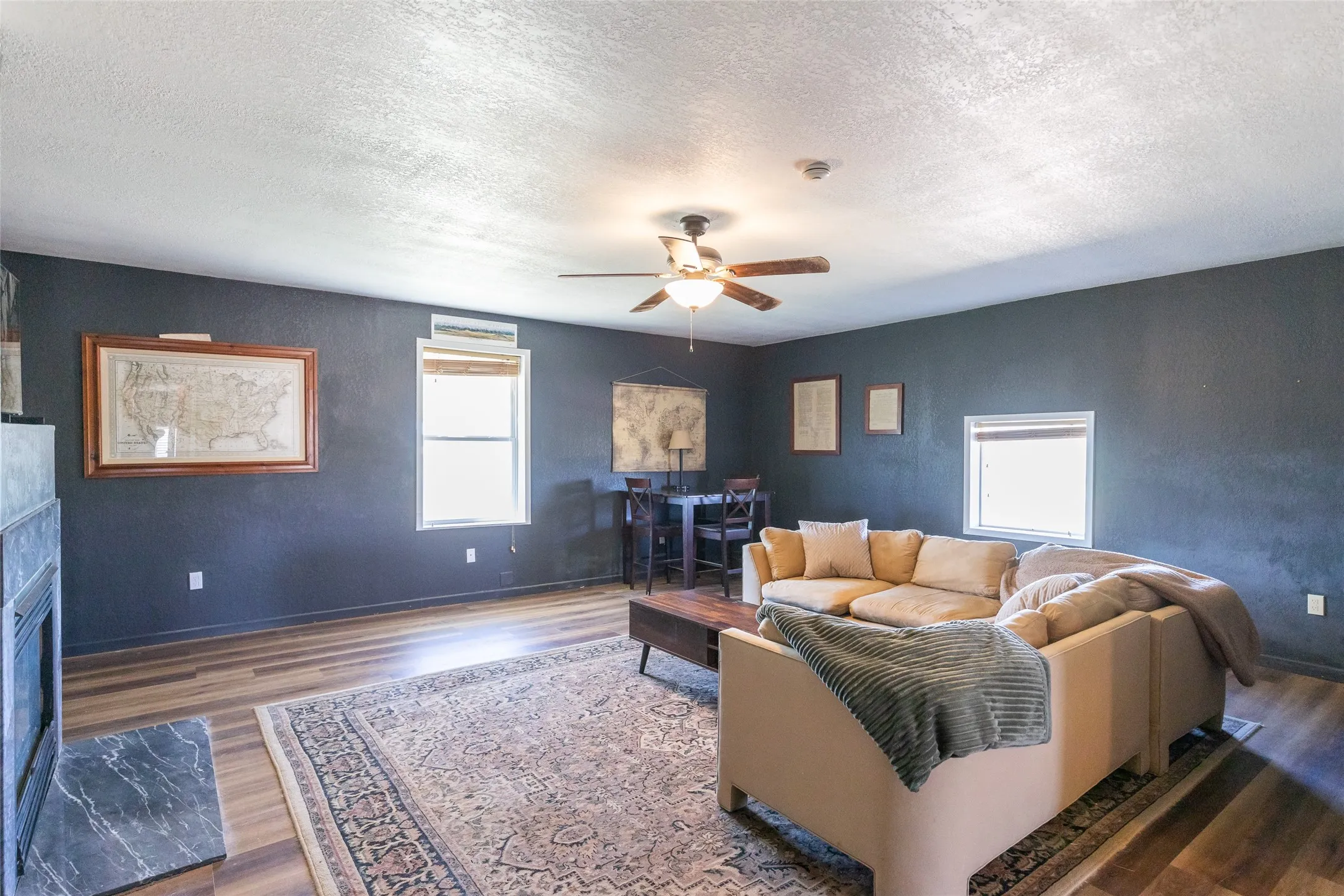Spacious living area featuring wood-finish flooring, dark accent walls, a ceiling fan, and multiple windows