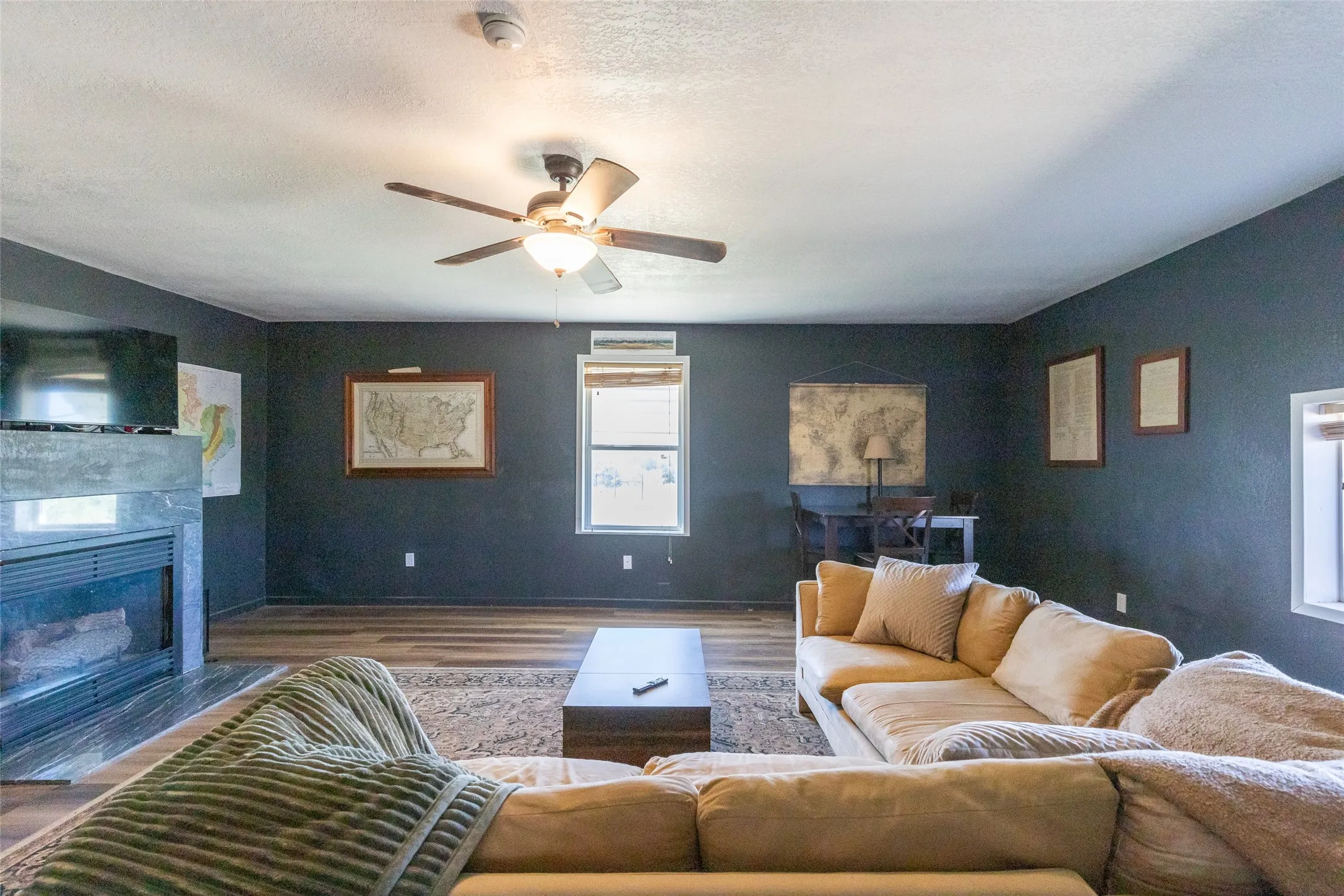 Spacious room featuring wood-finish flooring, dark accent walls, and a ceiling fan with integrated lighting