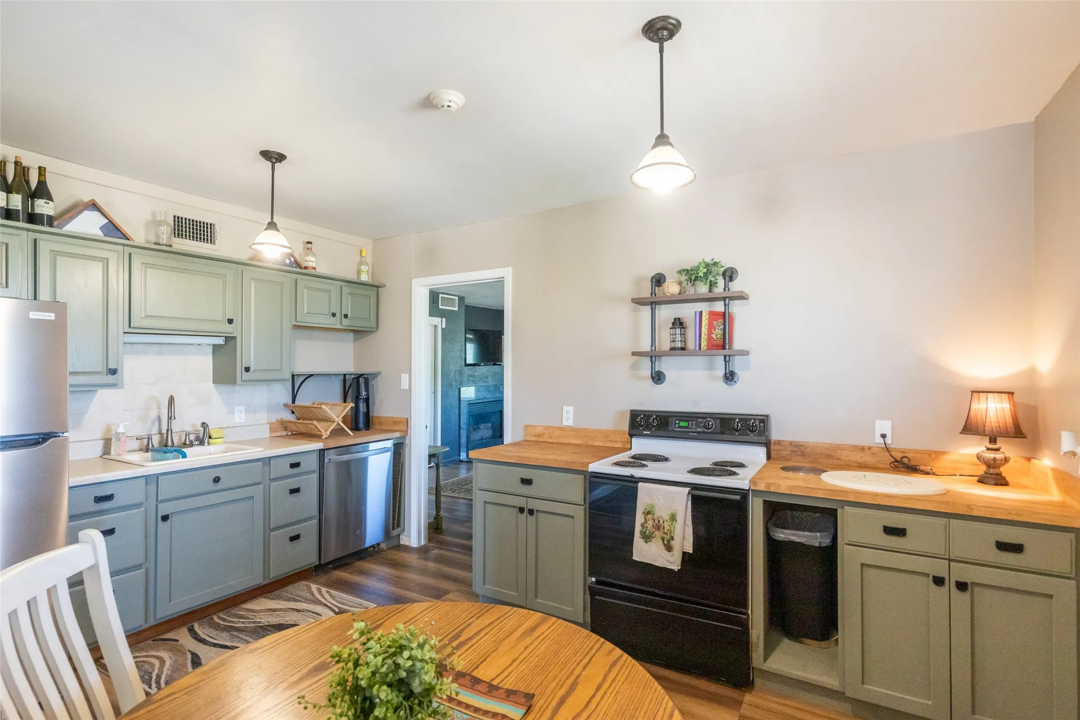 Kitchen featuring wood-finish flooring, light green cabinetry, light-toned countertops, a stainless steel refrigerator, and a built-in dishwasher