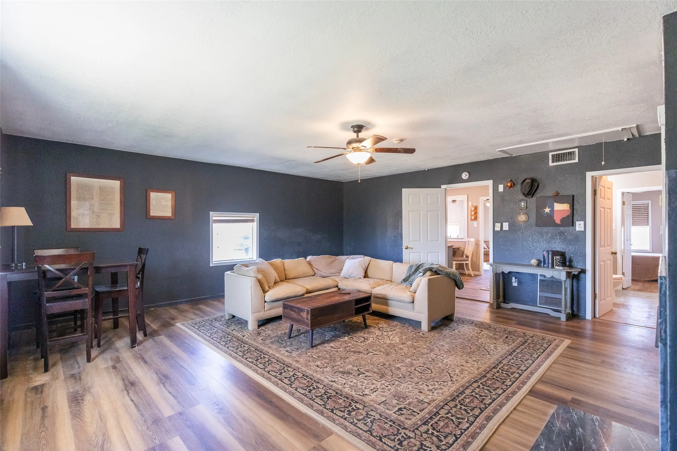 Spacious living area featuring wood-finish flooring, dark wall paint, and a ceiling fan with integrated lighting