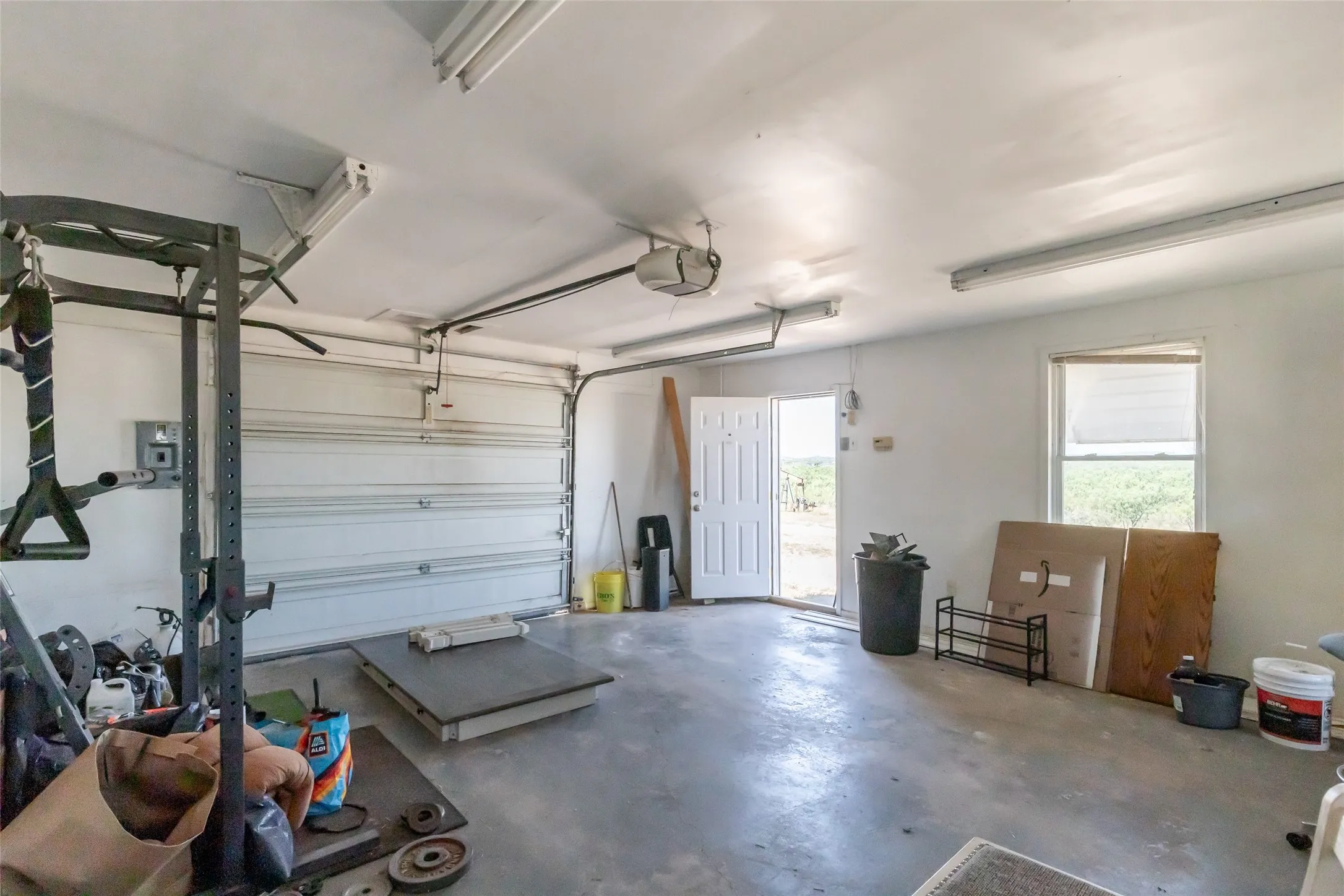 Spacious garage featuring a concrete floor, overhead fluorescent lighting, and a white paneled entry door