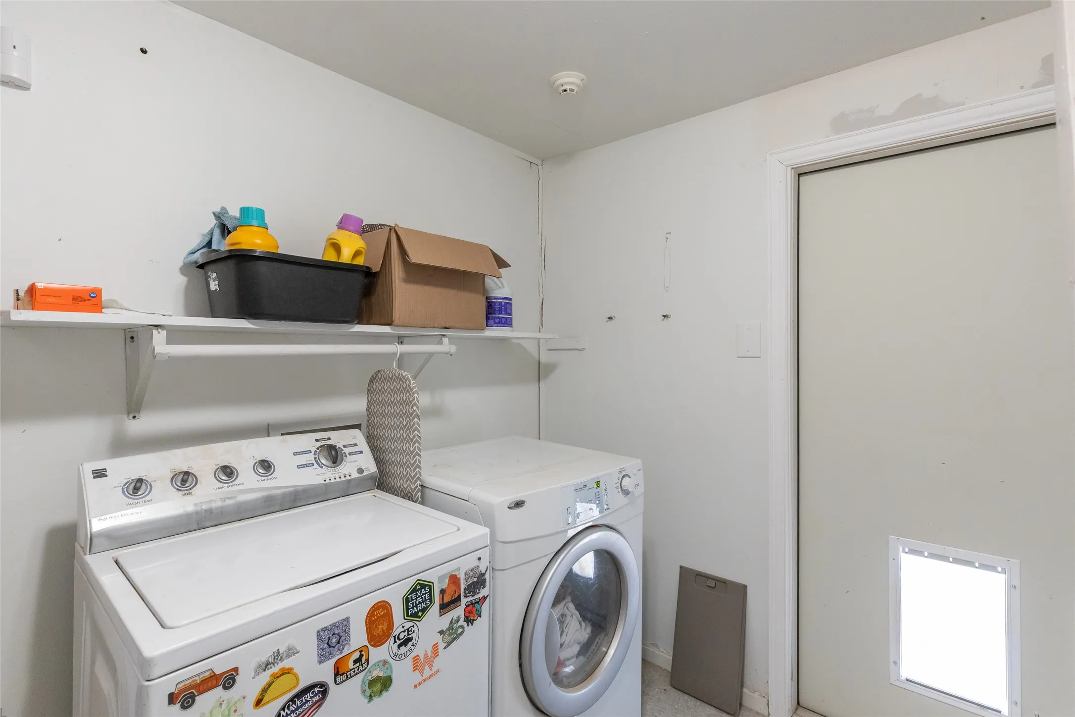 Dedicated laundry area featuring a white wall shelf for storage, a top-load washing machine, and a front-load washing machine
