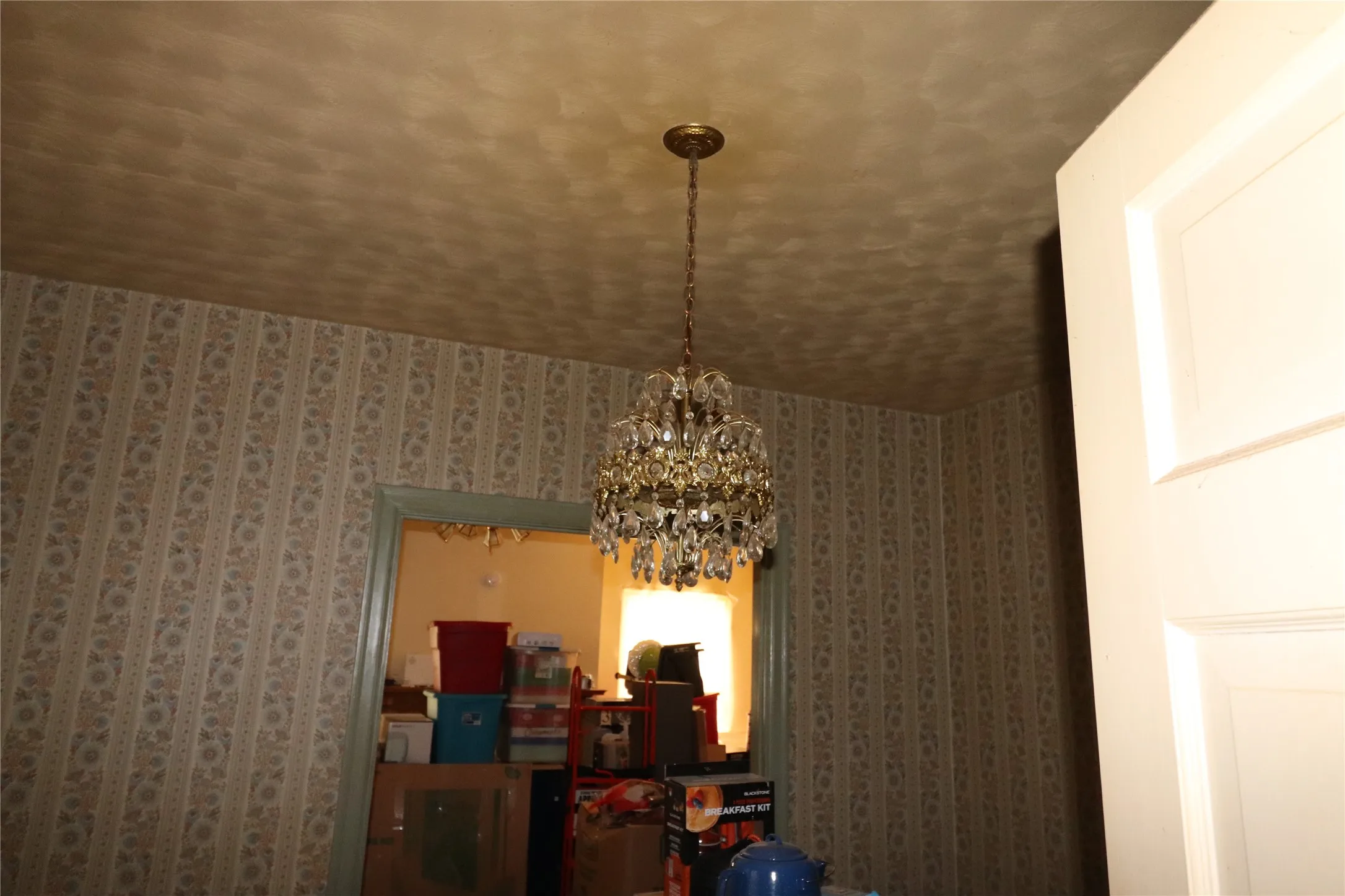 Ornate chandelier with crystal accents, patterned wallpaper, and a solid panel interior door