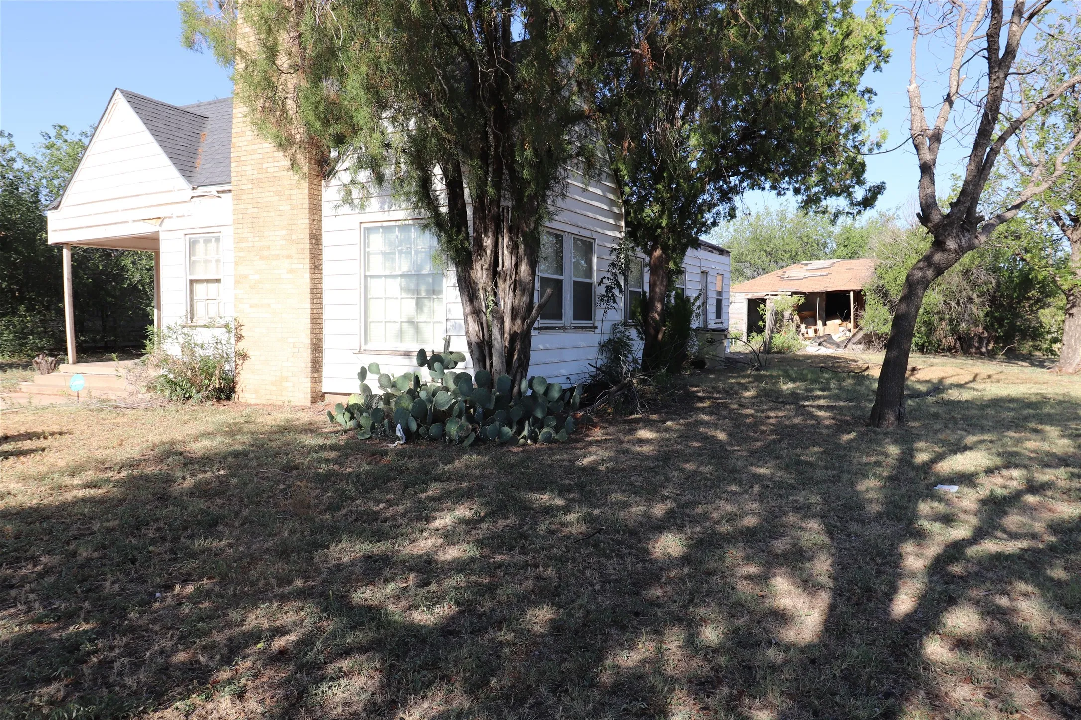 Exterior facade featuring white siding, a brick chimney, a covered porch, and mature landscaping