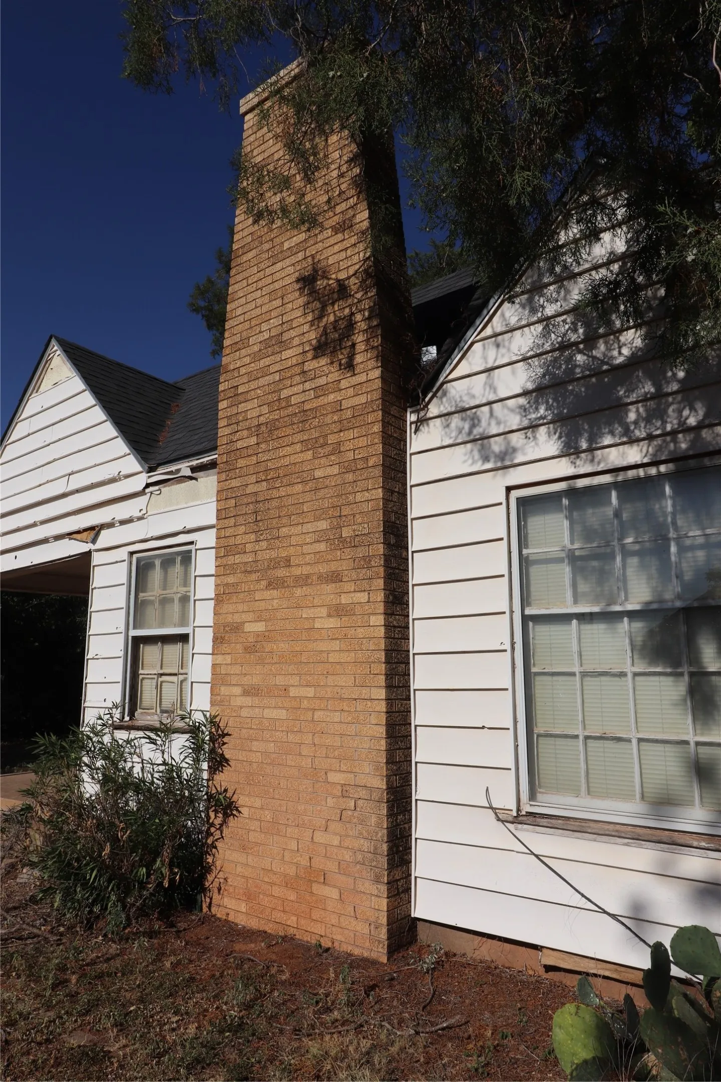 Brick chimney exterior with white horizontal siding and a dark shingled roof