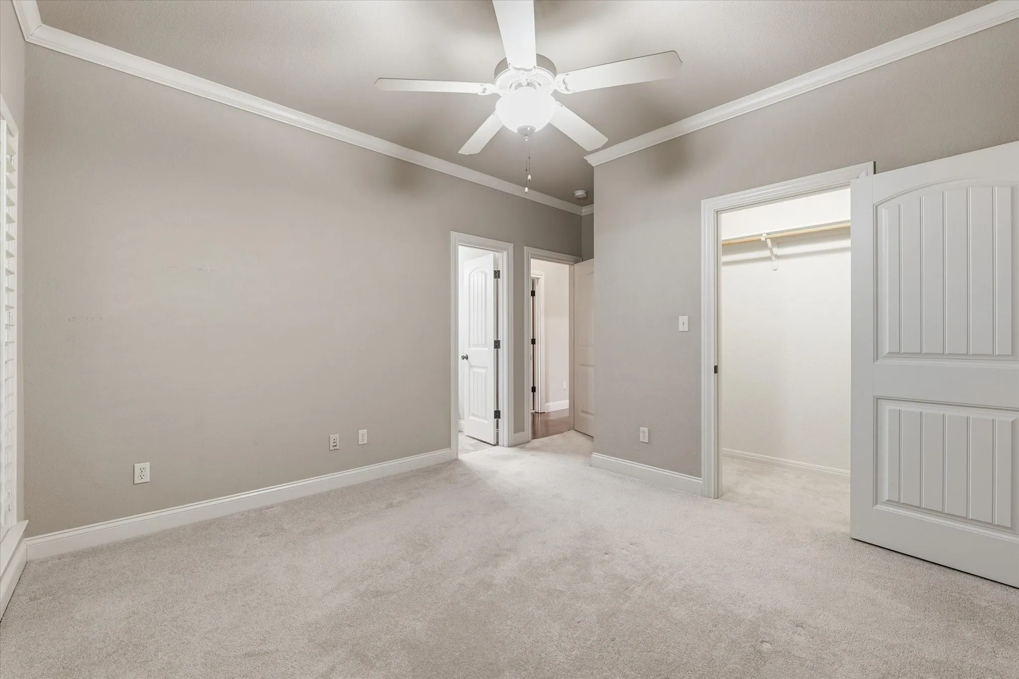 Carpeted room featuring a ceiling fan with light, crown molding, white baseboards, and a closet with bifold doors